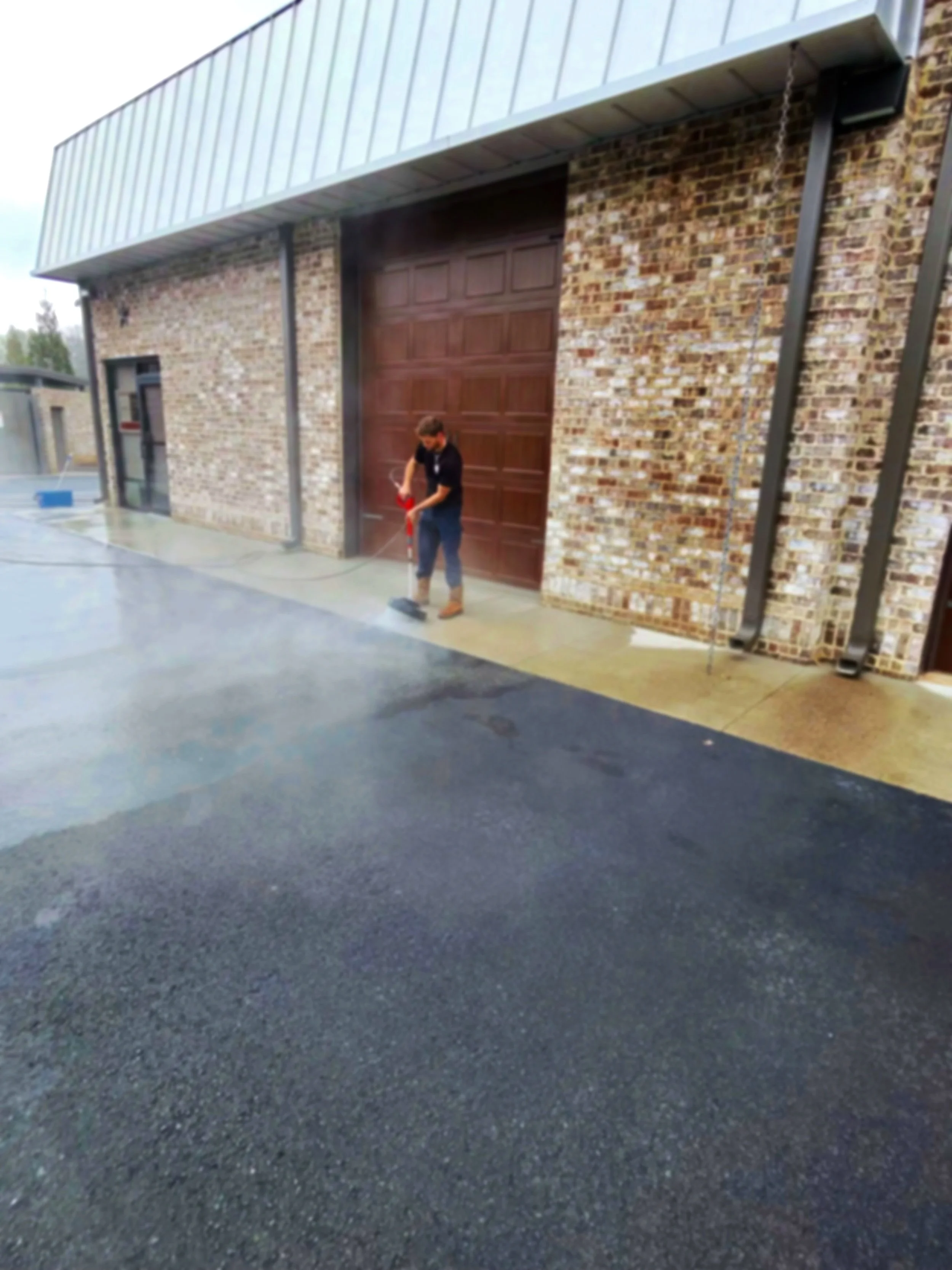 A person cleaning or washing the sidewalk in front of a brick building with a large wooden door.