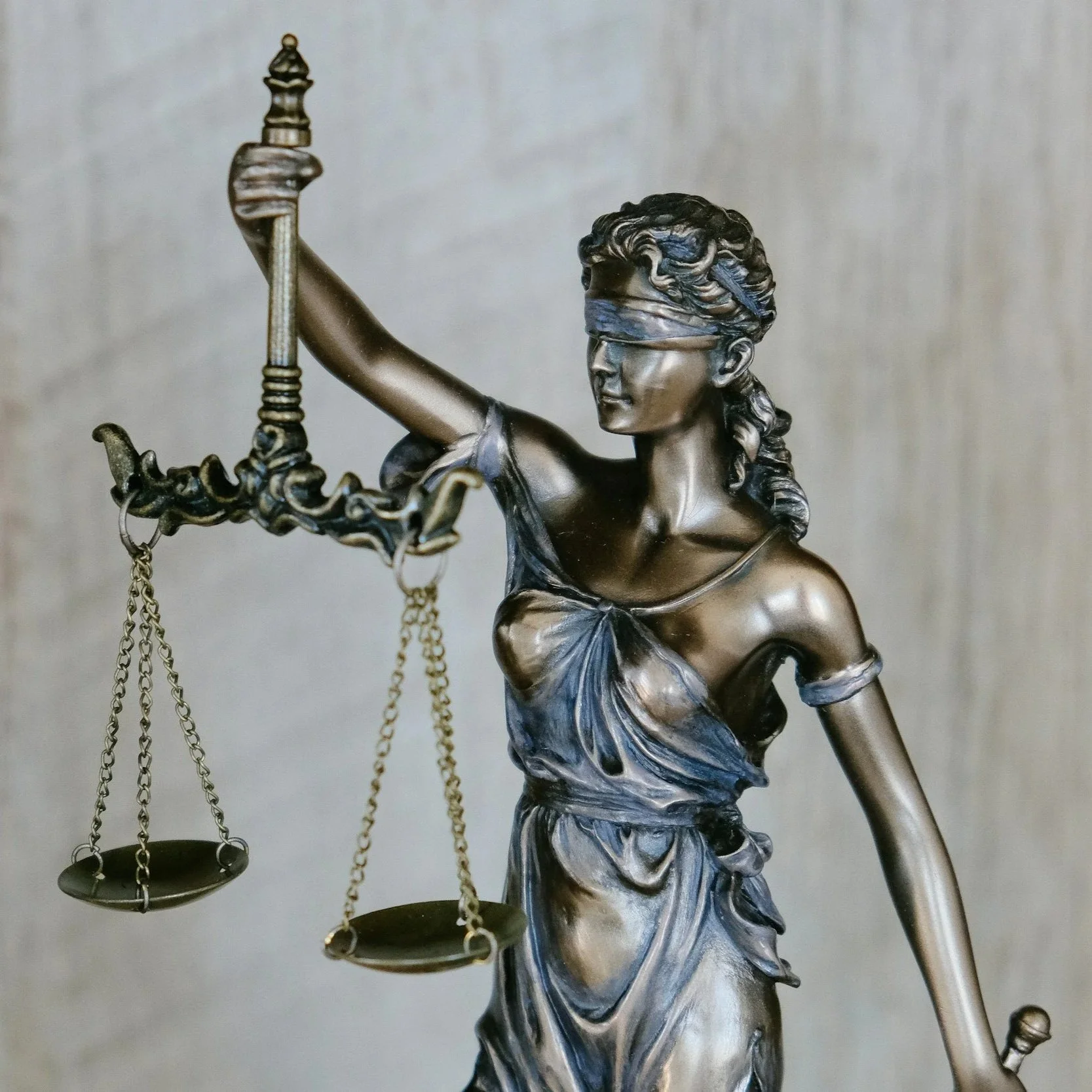 Close-up of a metallic statue of Lady Justice holding scales, with a blindfold over her eyes and a sword in her raised other hand.