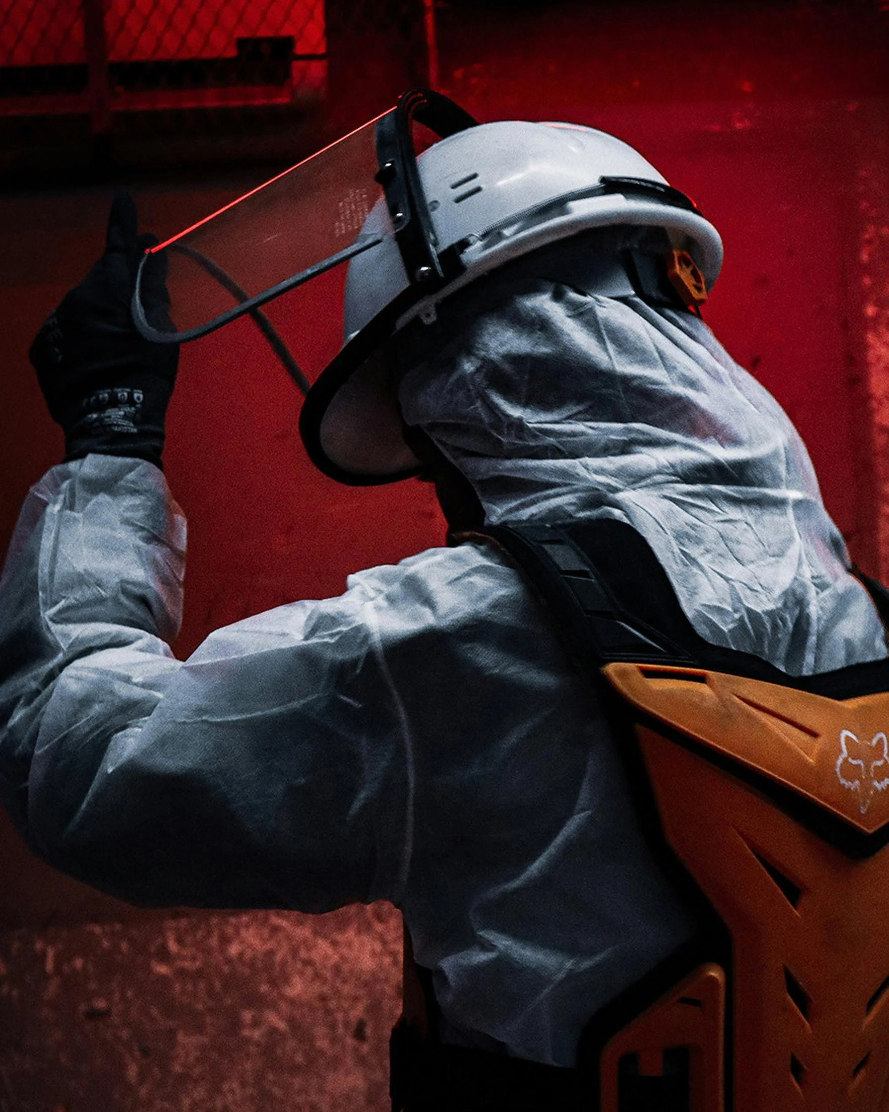 worker wearing gray protective suit, black gloves, and a hard hat, holding a laser device against a red background.