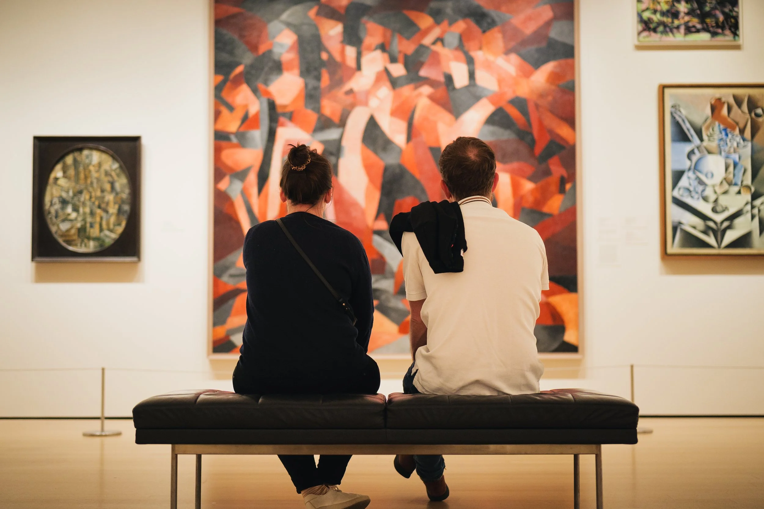 A couple sit at a bench observing artwork at the MoMA