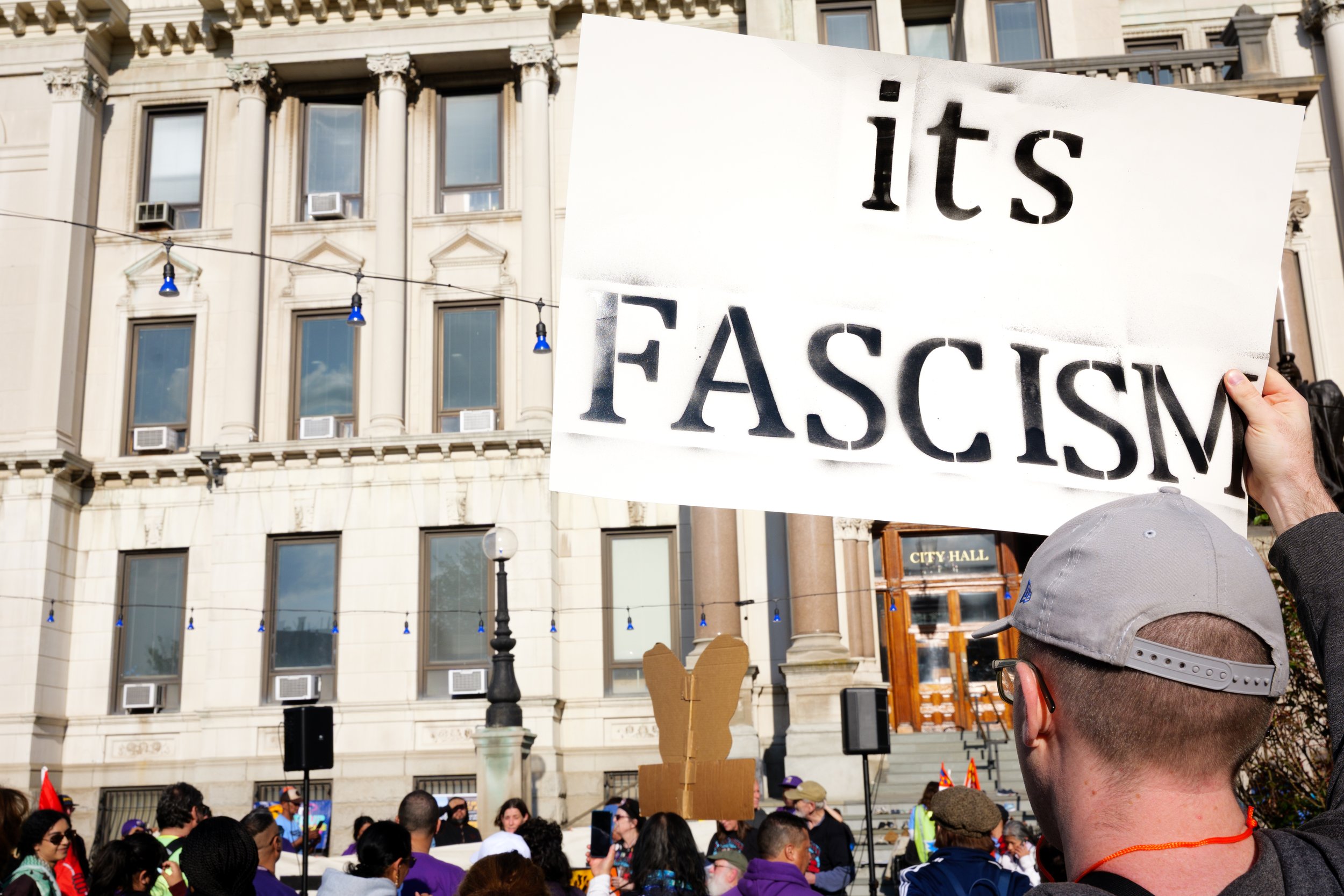 At the final stop of the May Day march in Jersey City, a protestor holds up a sign saying, "its FASCISM"