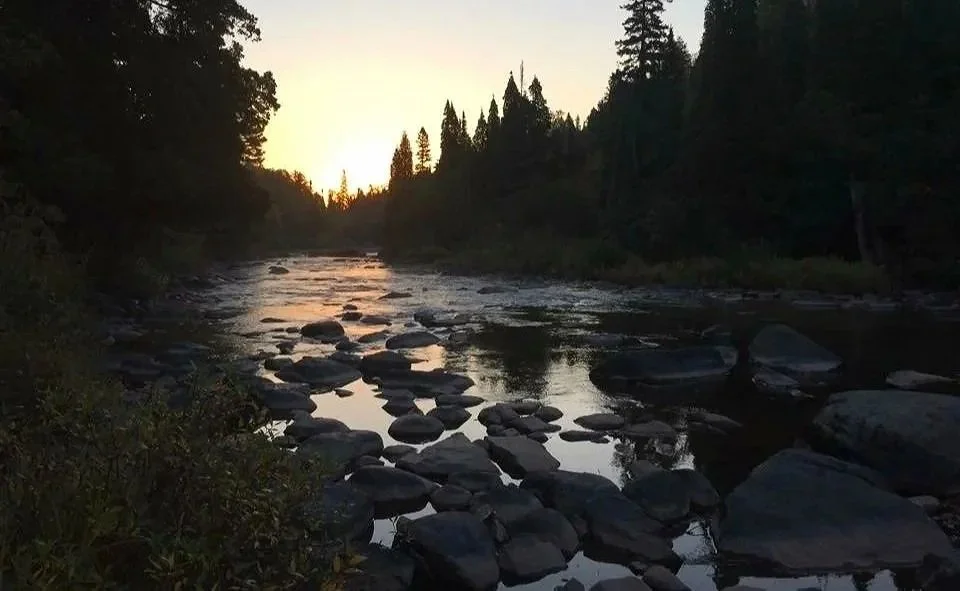 A river at sunset with rocks in the water and trees along the banks.