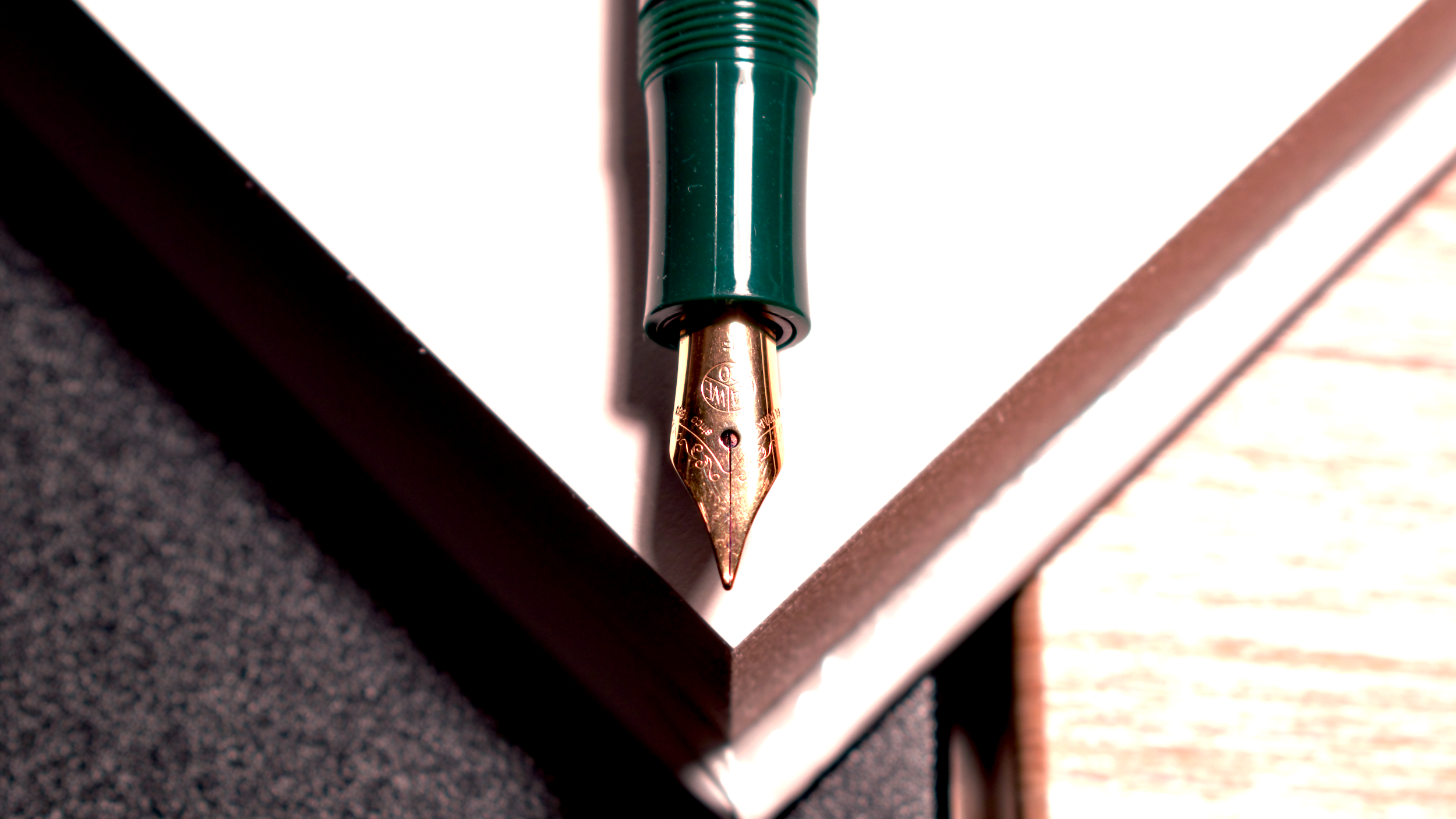 Close-up of a green fountain pen mounted on a white surface with a shadow cast on a textured black and brown gradient background.
