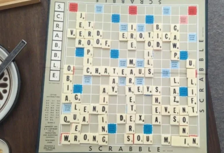 Close-up of a Scrabble game with tiles forming words like 'JET,' 'EDIT,' 'CITIES,' 'HATE,' 'BE,' 'AUTO,' 'GEARS,' and others on a game board.