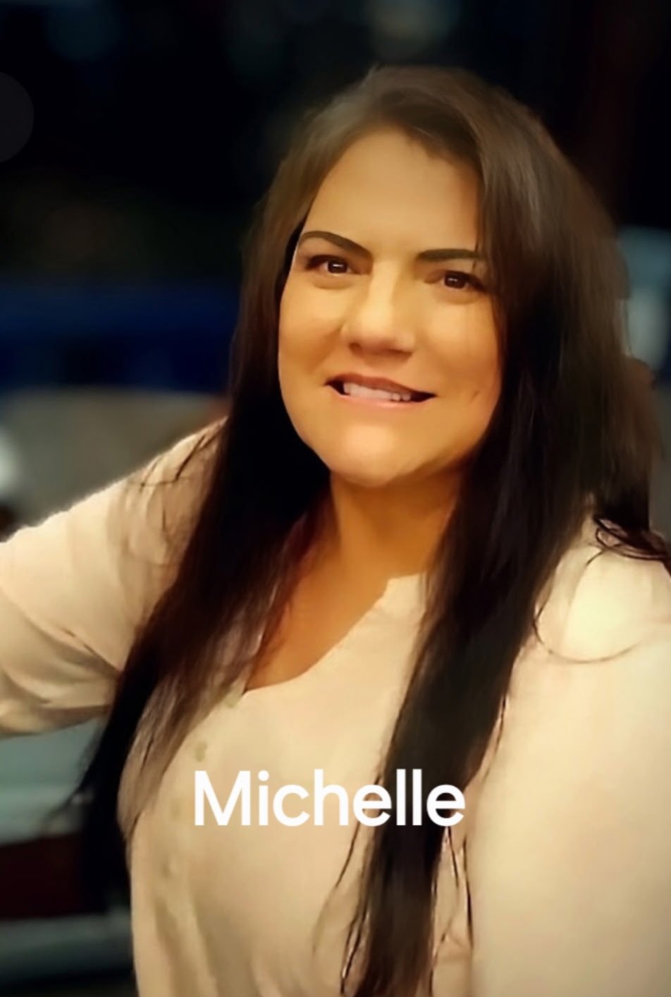 A woman with long dark hair smiling, wearing a light-colored top, with the name Michelle written at the bottom.