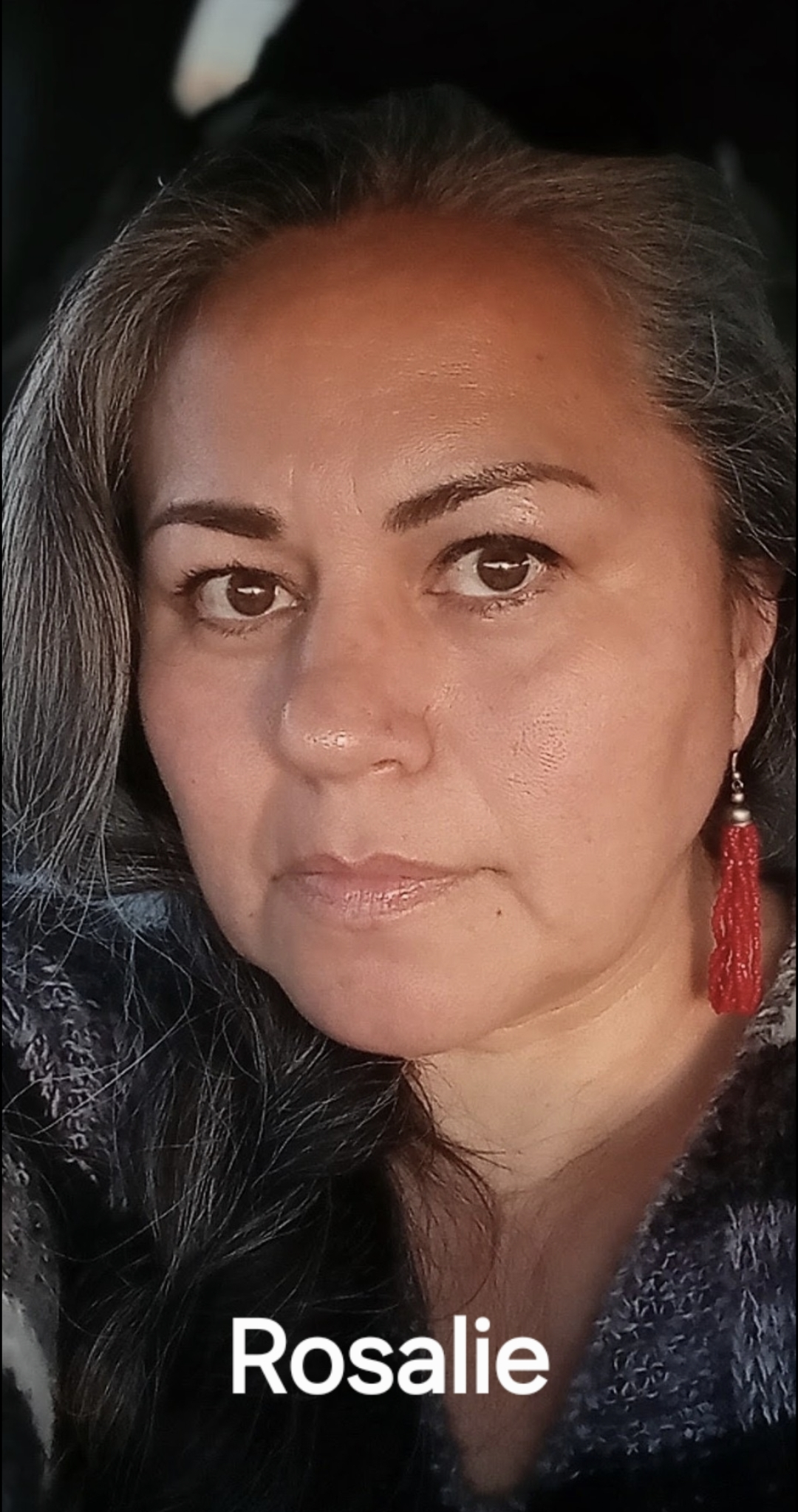 Close-up photo of a woman with long black hair, wearing a red earring, and a dark textured top, with the name 'Rosalie' written at the bottom.