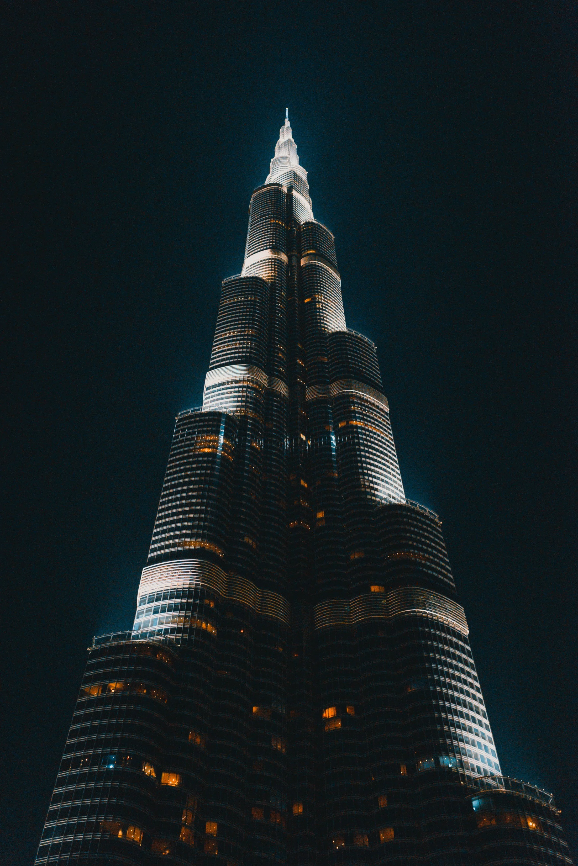 Night view of the illuminated Burj Khalifa skyscraper in Dubai from a low angle, with a dark sky background.