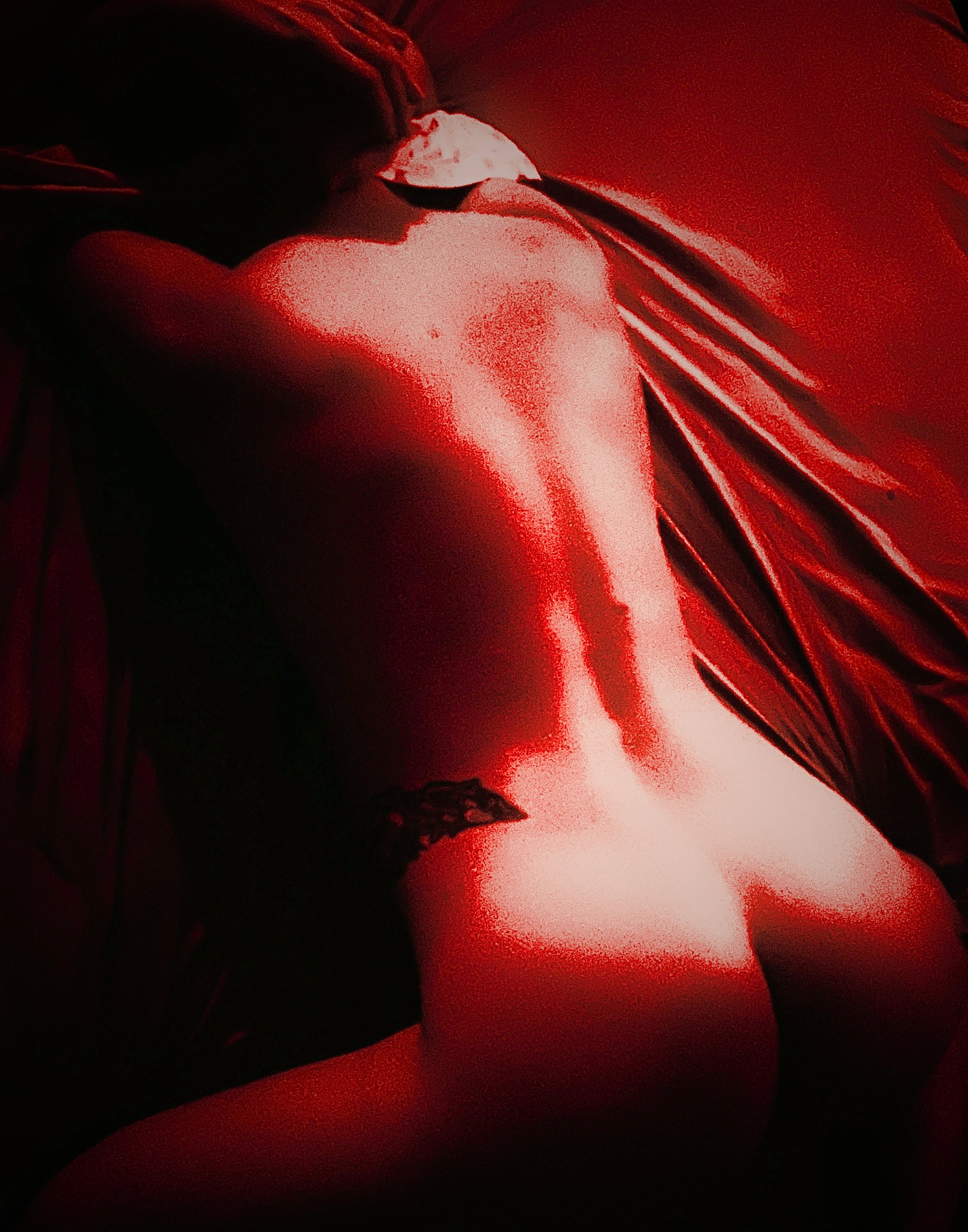 A woman lying on a bed in a dark room illuminated by red lighting, A red aesthetic nude figure photograph featuring a woman in an erotic pose, with red lighting.