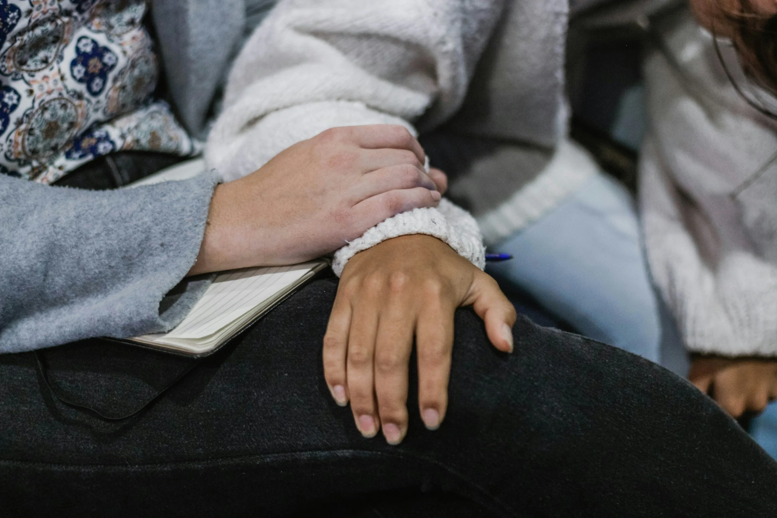 A person is holding another person's hand on their lap during a meeting or event.