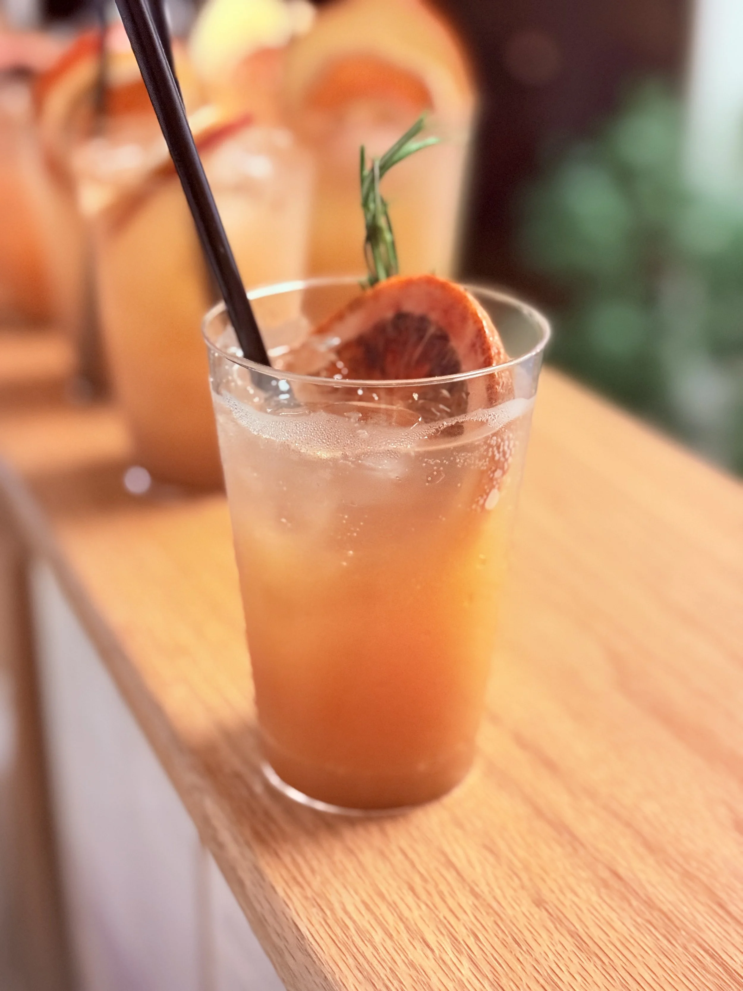 A tall glass of iced peach tea garnished with a slice of peach and a sprig of rosemary, with a black straw, placed on a wooden surface.