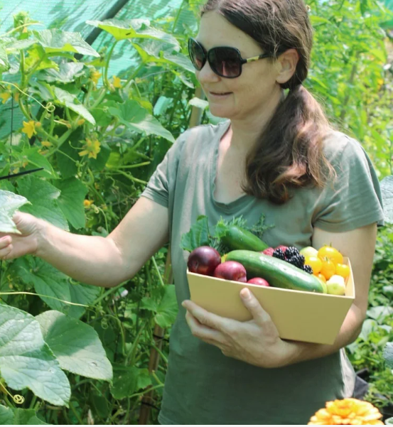 Kelly from Nature Thrives holding a basket of homegrown vegetables in a productive food garden.