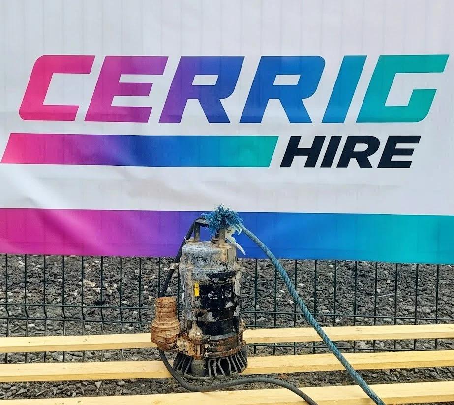 Construction site with a sign reading 'CERRIG HIRE' and a power tool on a wooden platform in front of a fence.