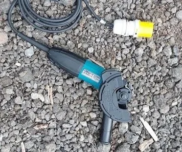 A power drill and a small white bottle on gravel ground.