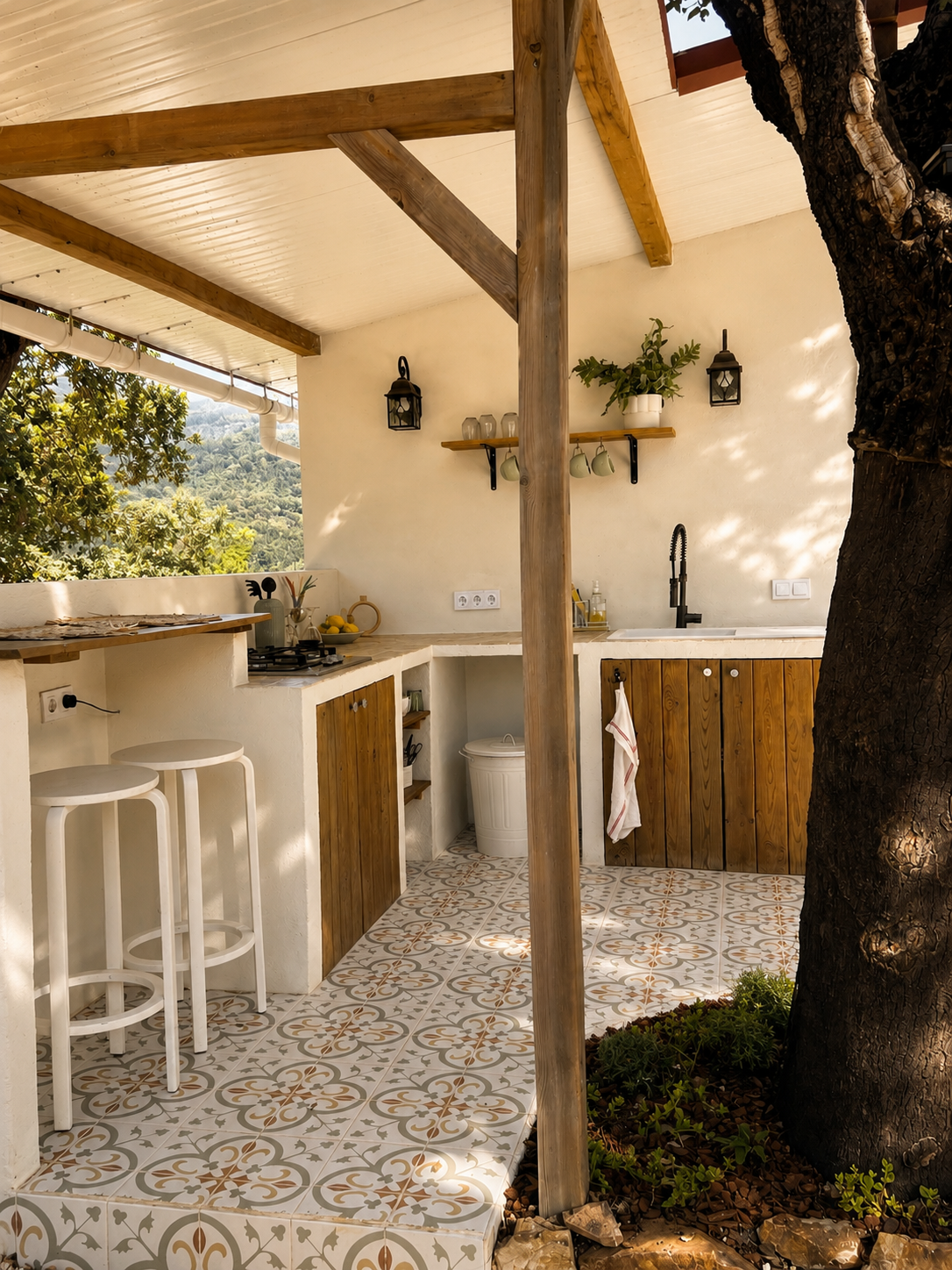 Outdoor kitchen with patterned tile floor, wooden cabinets, and a countertop with a stove, lemons, and various kitchen utensils. There are two white stools, a wall shelf with cups and a potted plant, and a large tree growing nearby. The area has a ro
