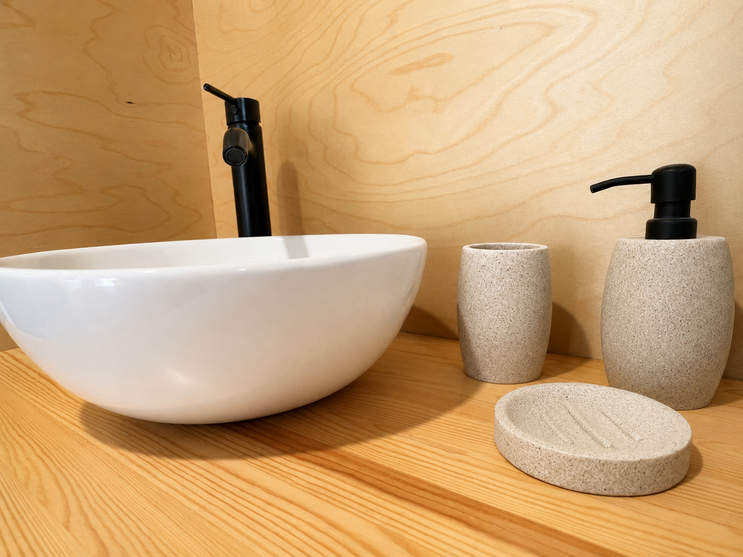Bathroom vanity with a white oval vessel sink, black faucet, and beige textured soap dispenser, toothbrush holder, and soap dish on a wooden countertop.