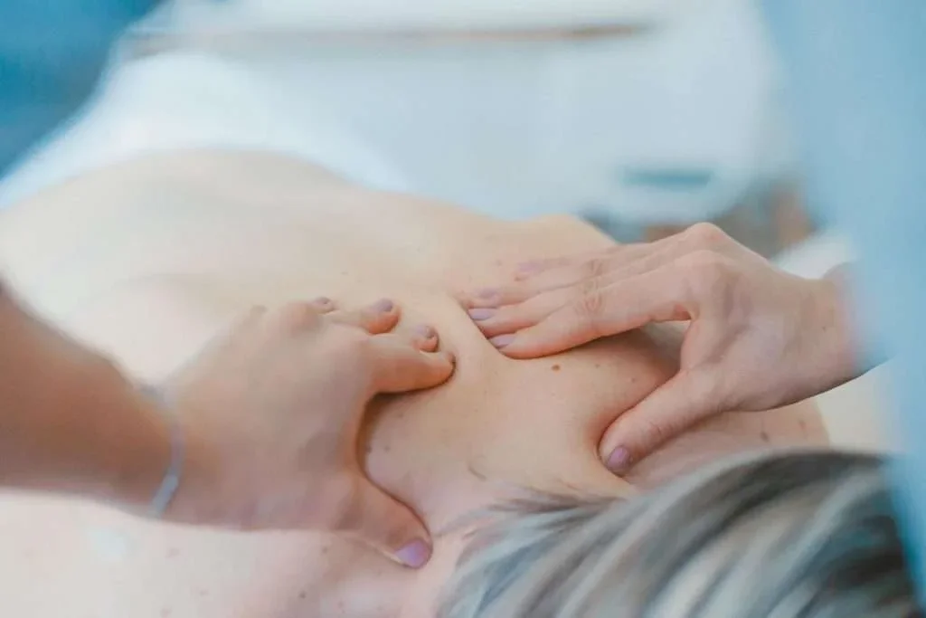 A person receiving a massage on their back with several hands applying pressure.