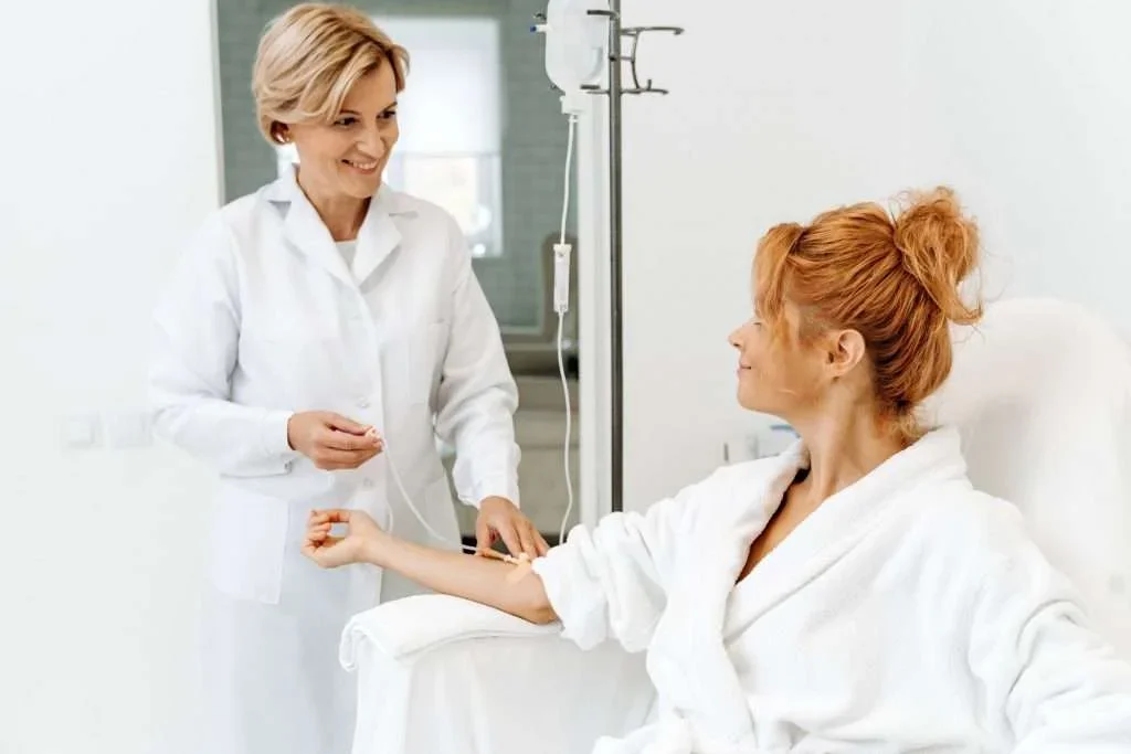A nurse or healthcare professional drawing blood from a smiling woman patient in a hospital or clinic room.