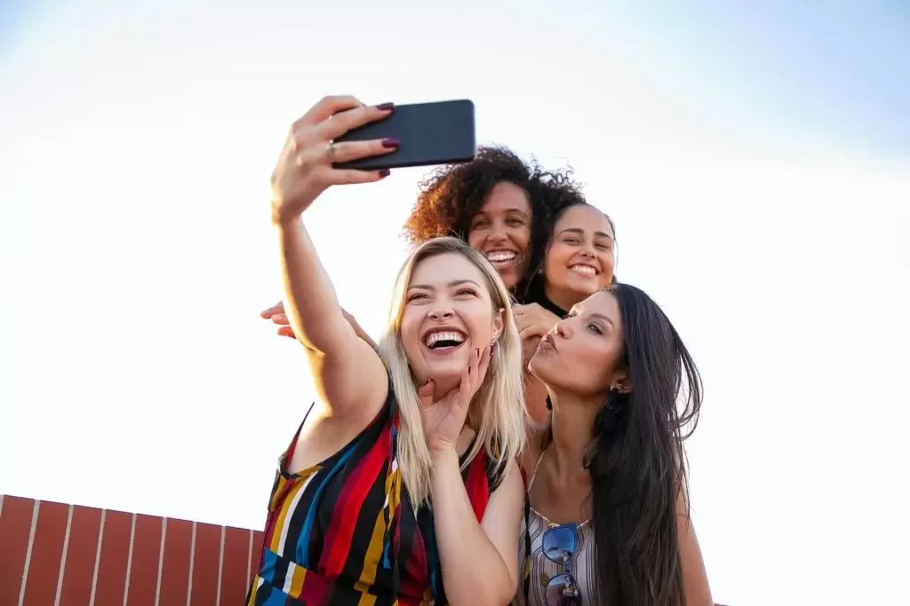 Four diverse women taking a selfie together outside, smiling and having fun.