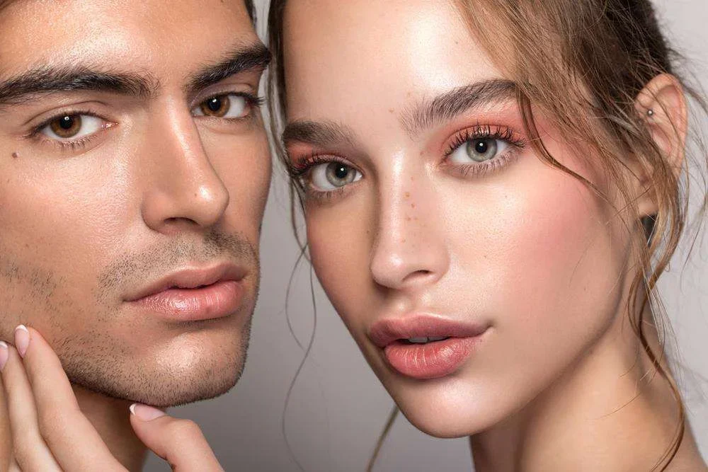 Close-up of a man and woman with clear skin and light makeup, looking at the camera.