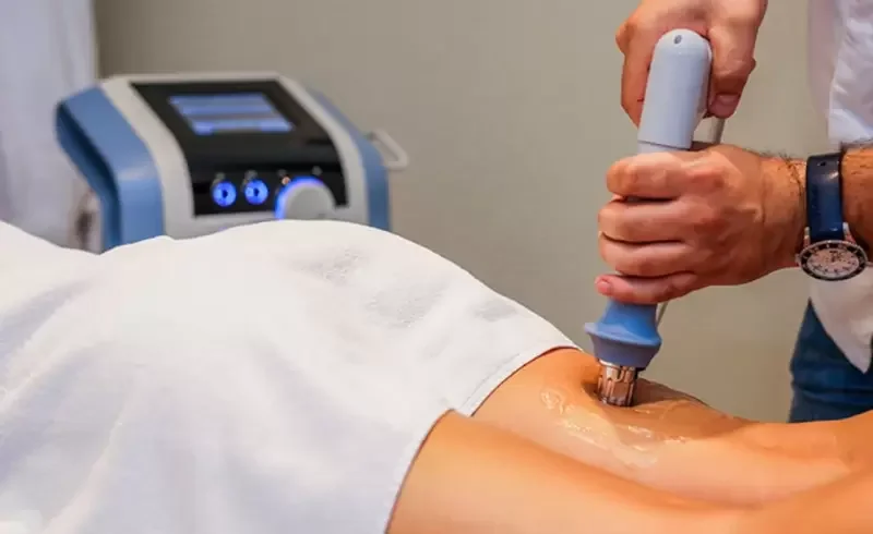 A medical professional performing a procedure using a handheld device on a patient's knee in a clinical setting.