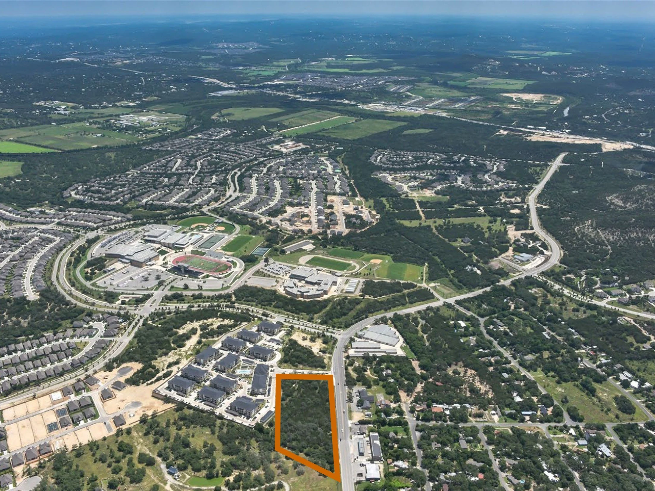 Aerial view of a suburban area with residential houses, green fields, and roads, taken from a high altitude with a clear sky.
