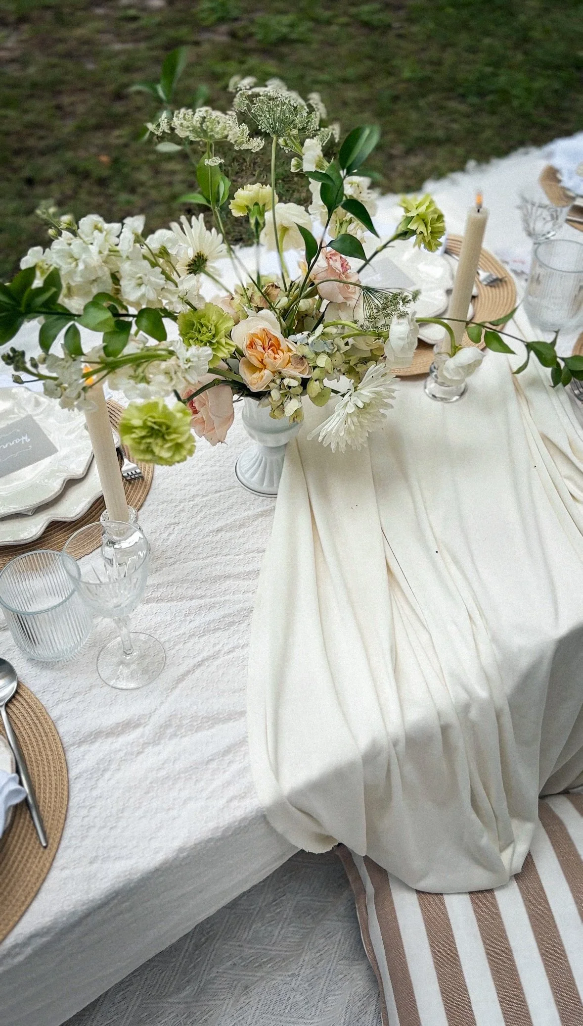 A table set for a meal with a white tablecloth, a floral centerpiece, candles, glassware, and place settings.