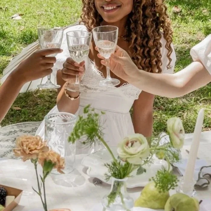 People outdoors toasting with glasses of  champagne at a celebration table decorated with flowers.