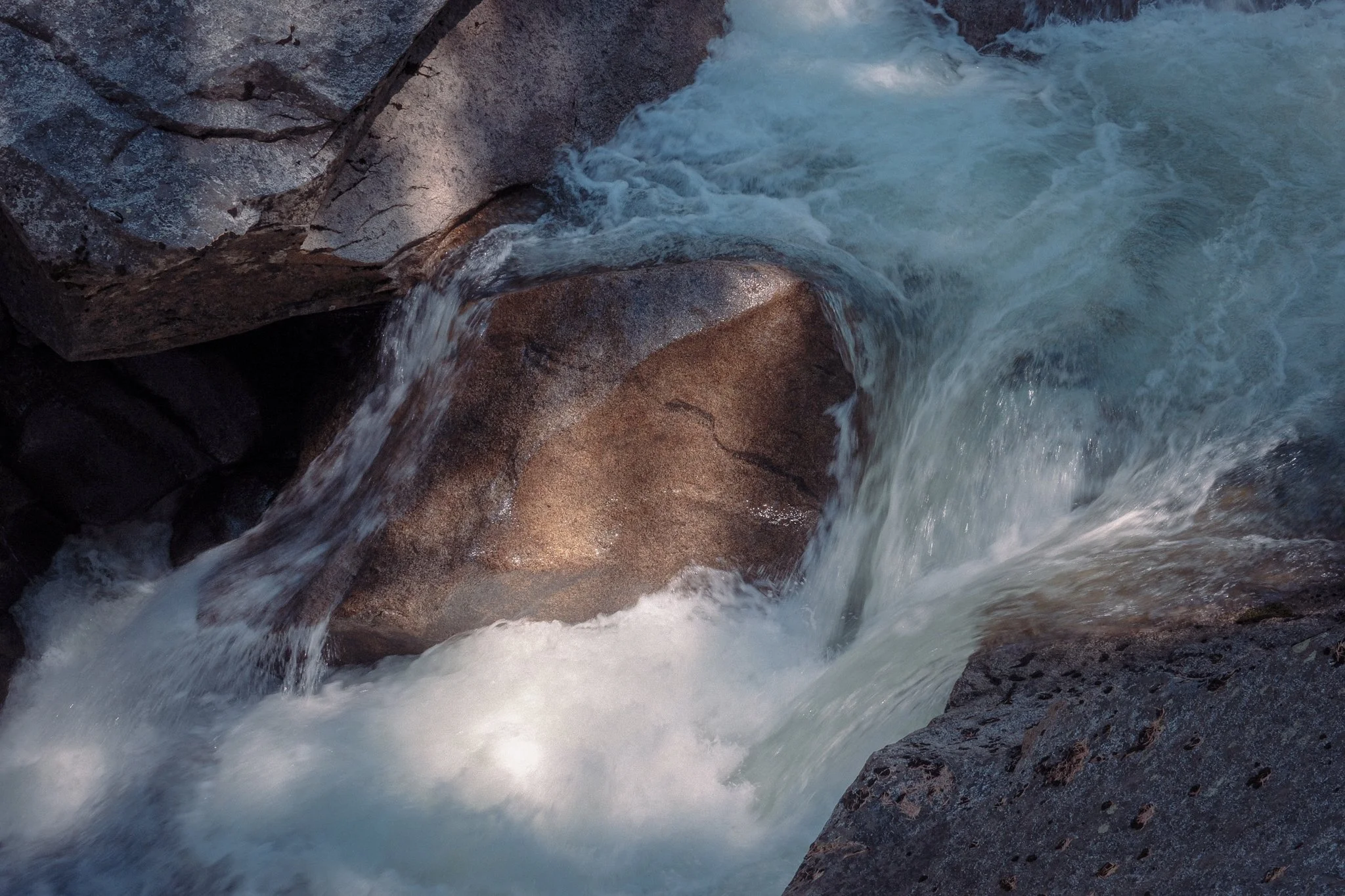 Close-up of a rapid flowing stream over large rocks in a natural setting.