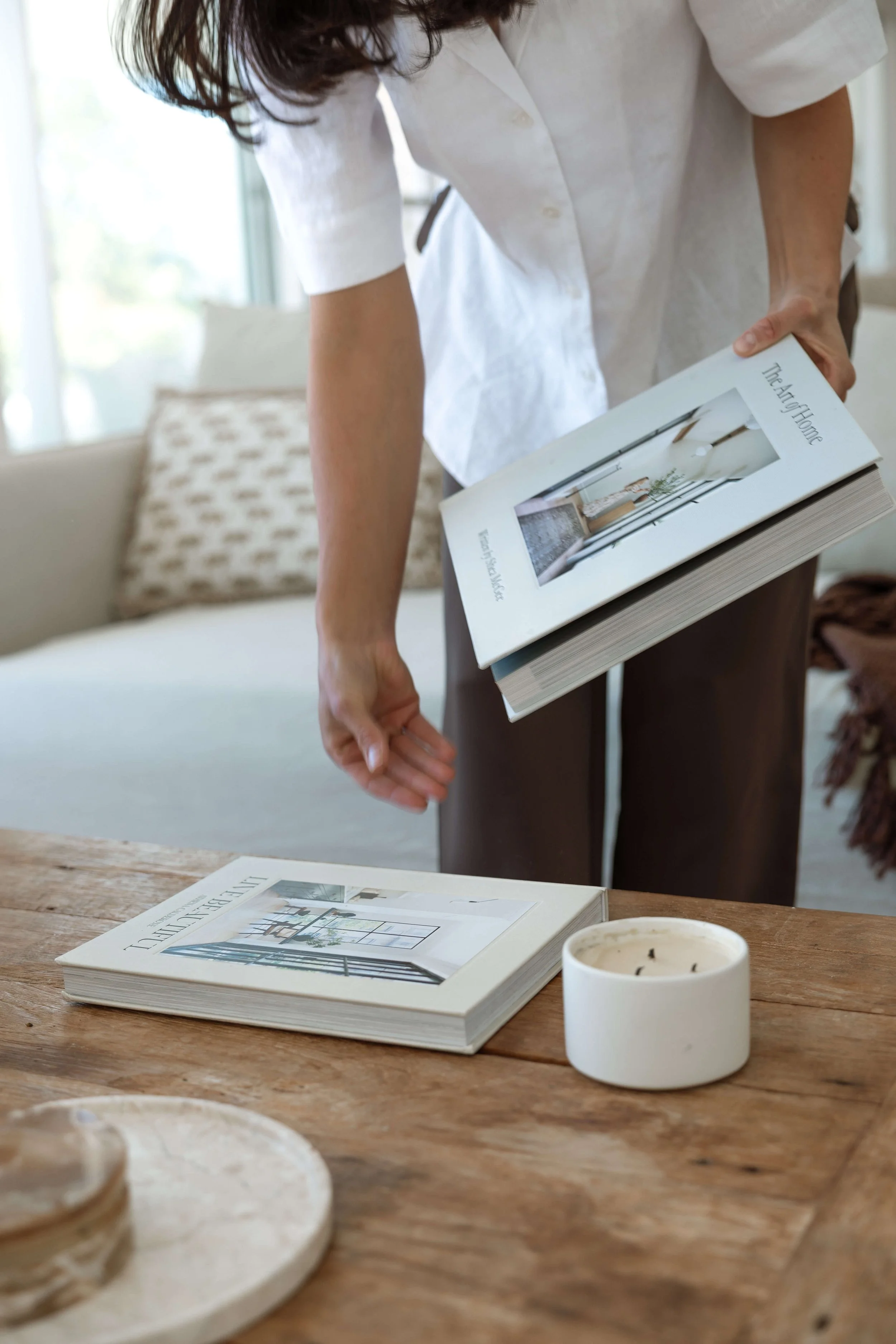 A woman in a white shirt holds a book titled 'The Art of Home' with a photo of a modern, bright interior on the cover.