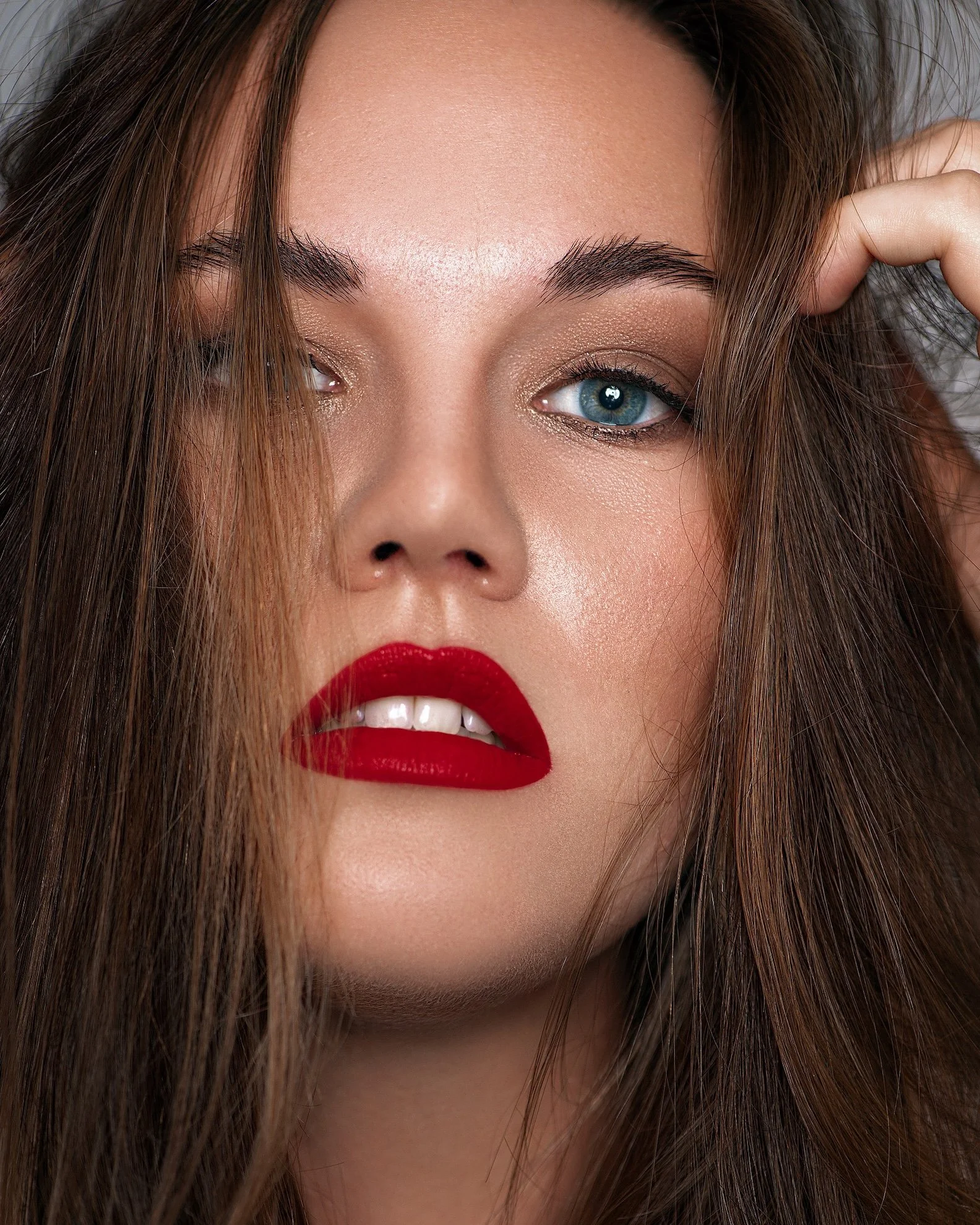 Nahaufnahme eines Frauen Gesichts mit roten Lippen, blauen Augen, braunen Haaren und makeup.