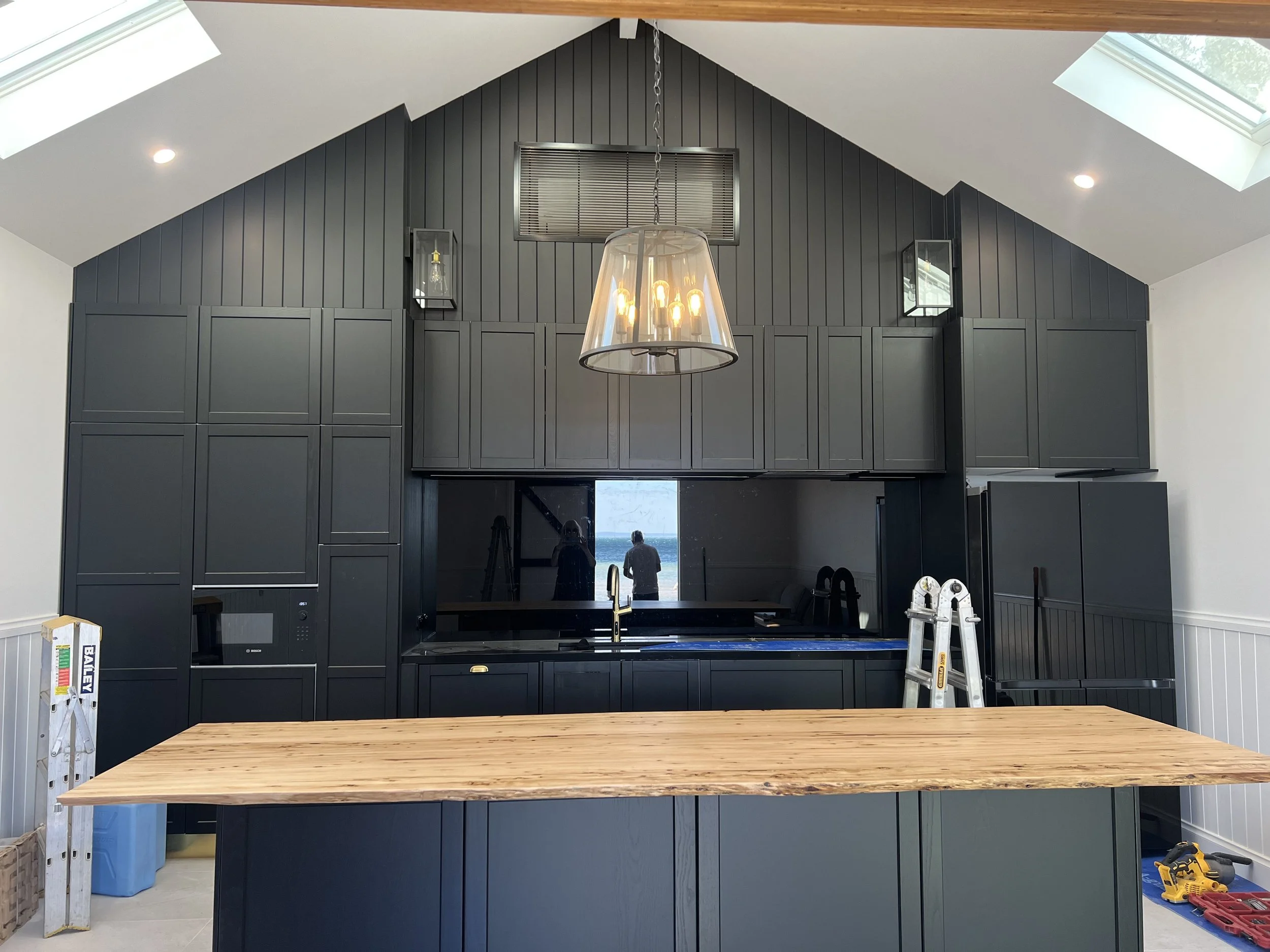 Boatshed kitchen and bar with dark cabinetry and timber bench