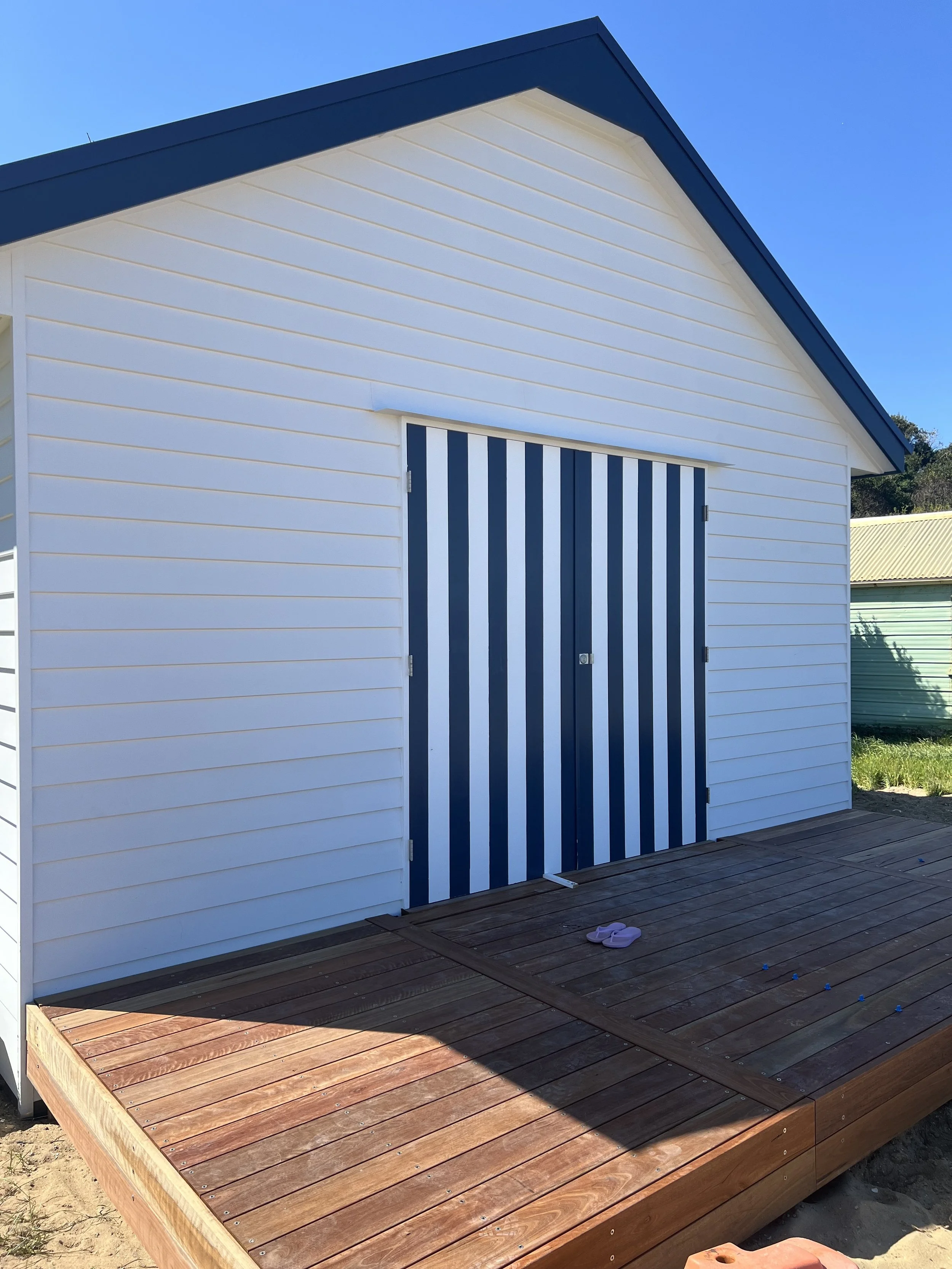 Rebuilt boatshed with white weatherboards and striped doors