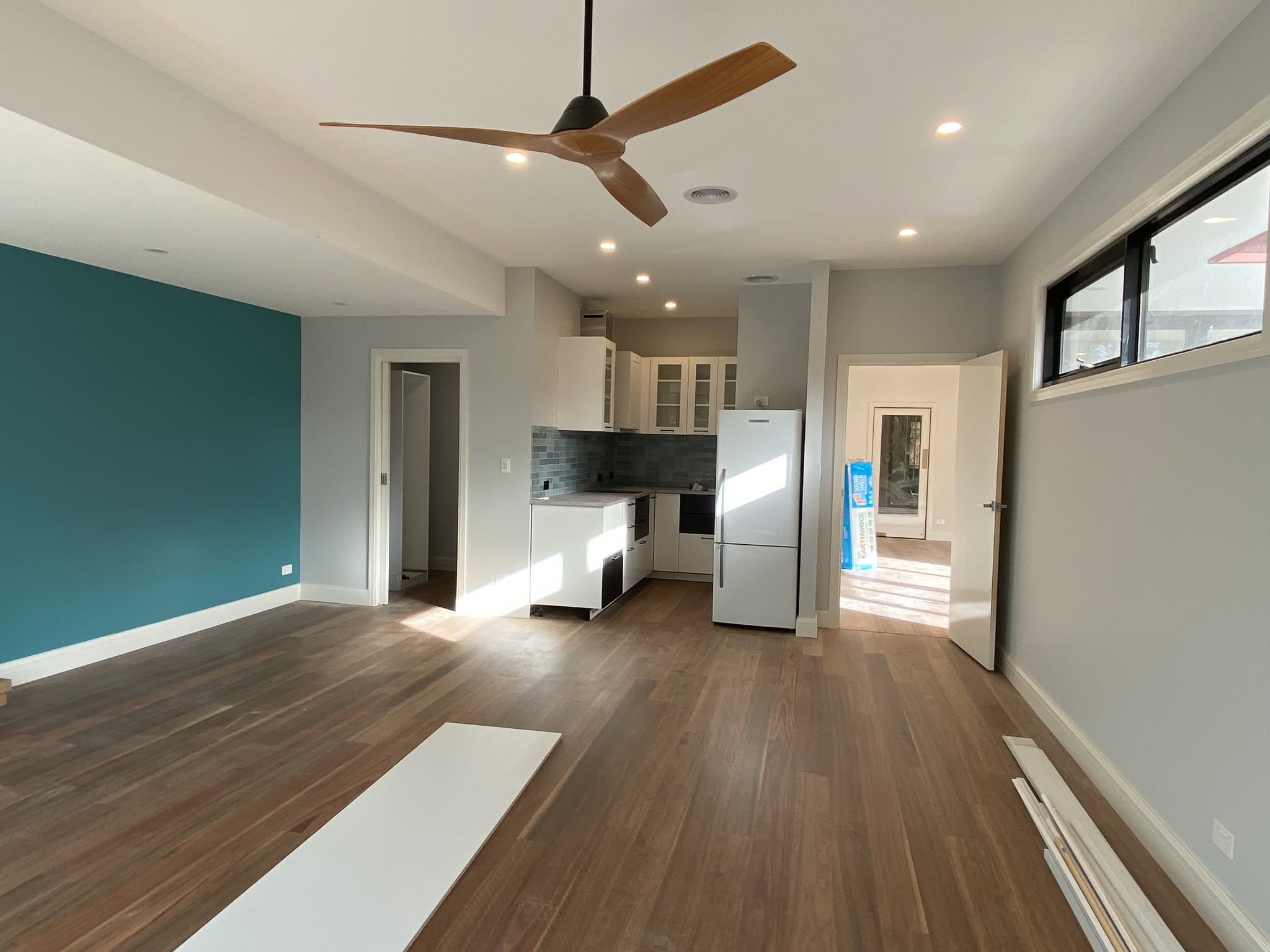 Self-contained unit at the rear with timber floors, a ceiling fan, a teal feature wall and a compact kitchen