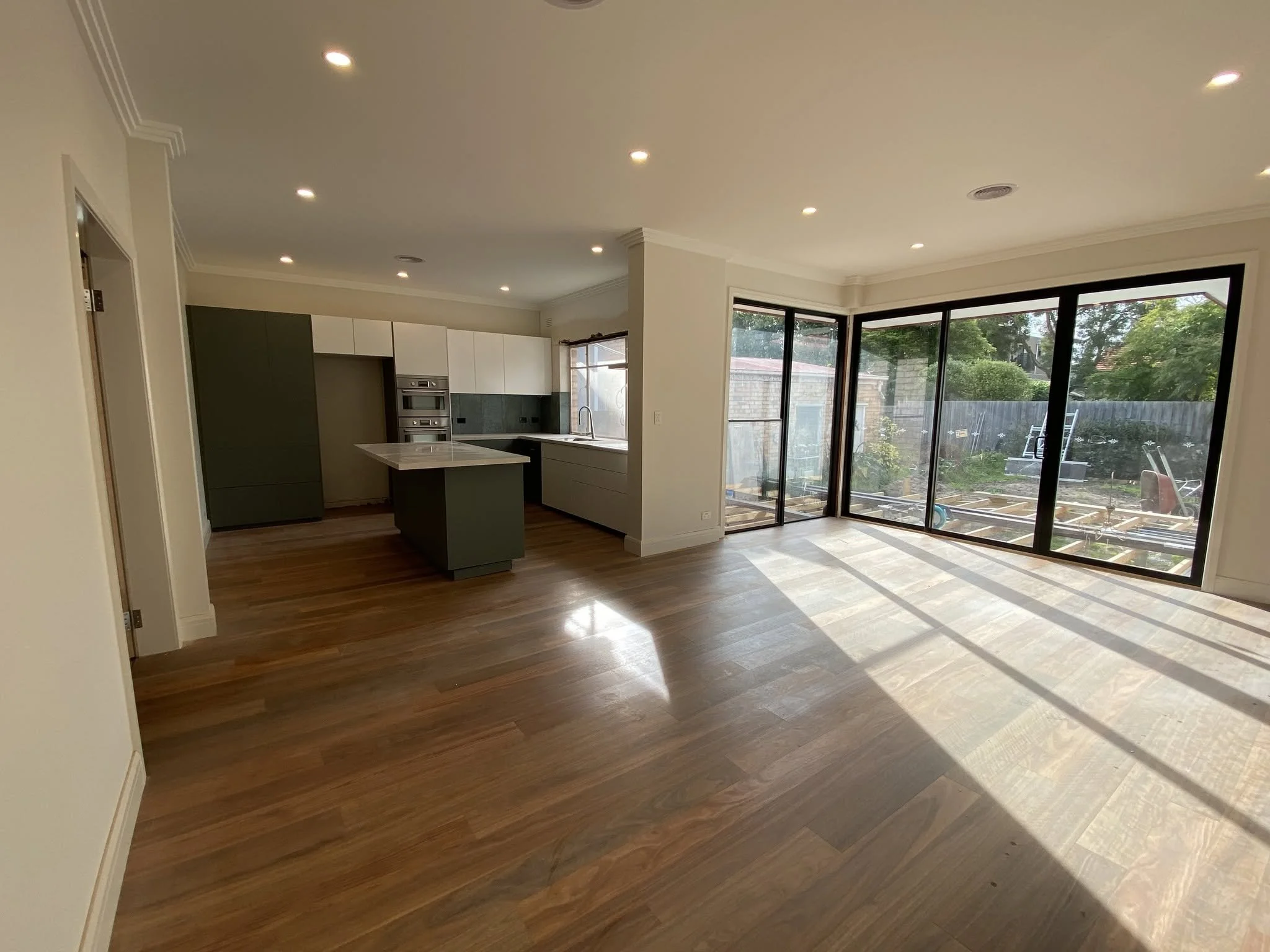 New open-plan kitchen and dining area with a dark island bench, timber floors and full-height sliding doors to the backyard