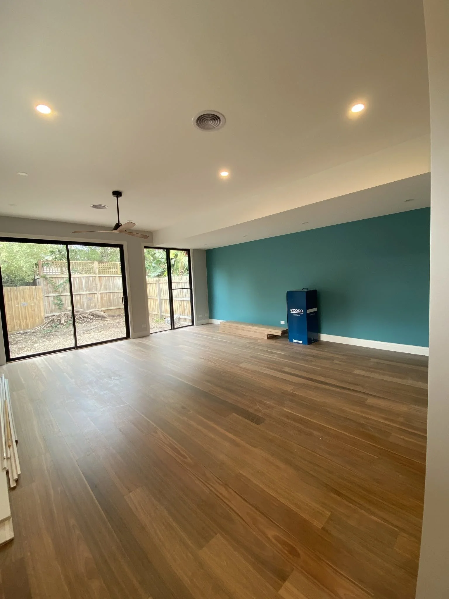 New open-plan living area with timber flooring, downlights, a teal feature wall and sliding doors to the garden