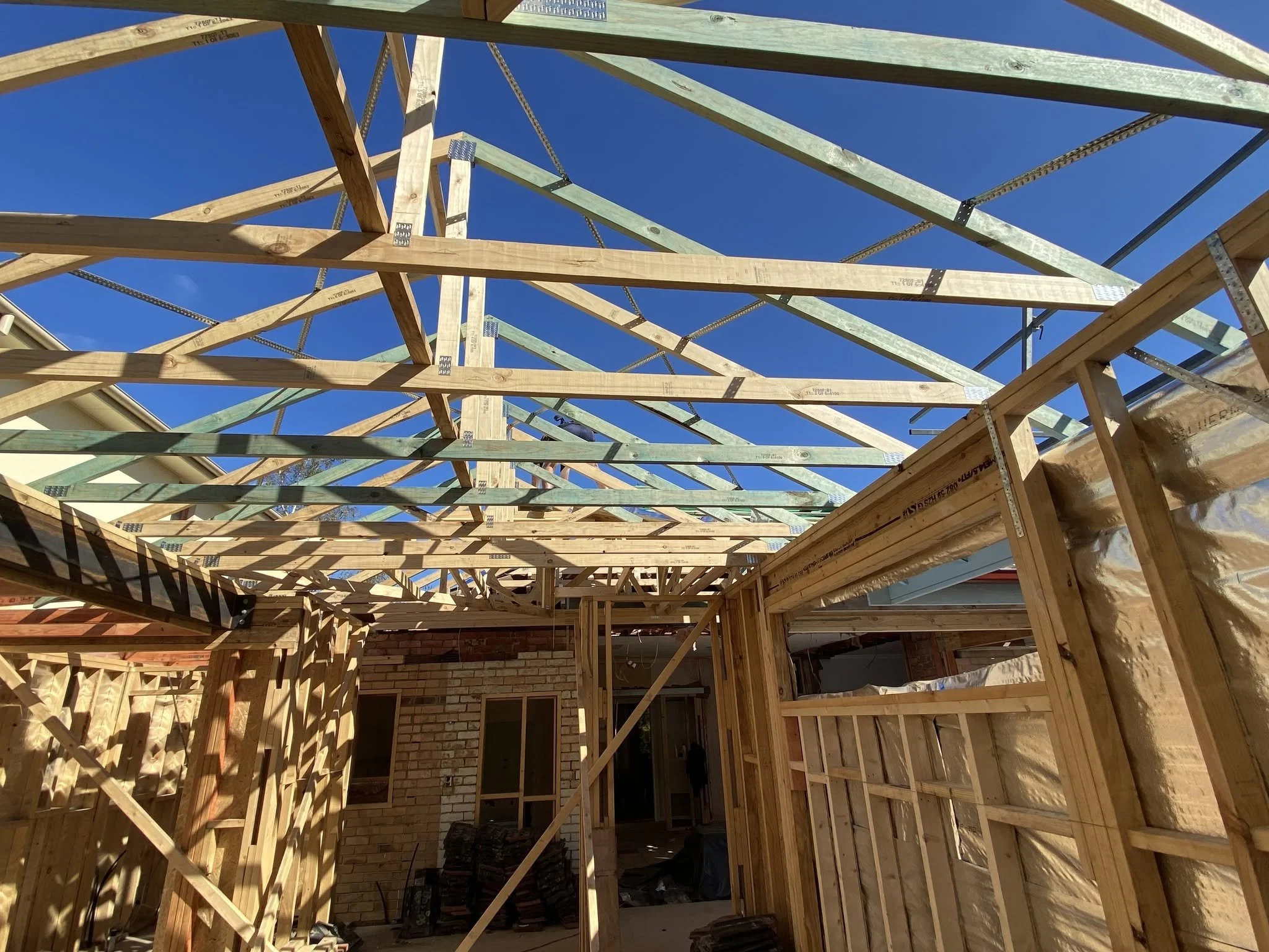 New timber wall frames and roof trusses for the McKinnon extension against a blue sky