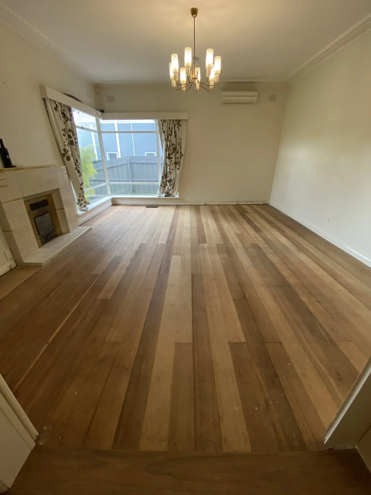 Refinished lounge with new timber floorboards, a chandelier and a bay window in the McKinnon home