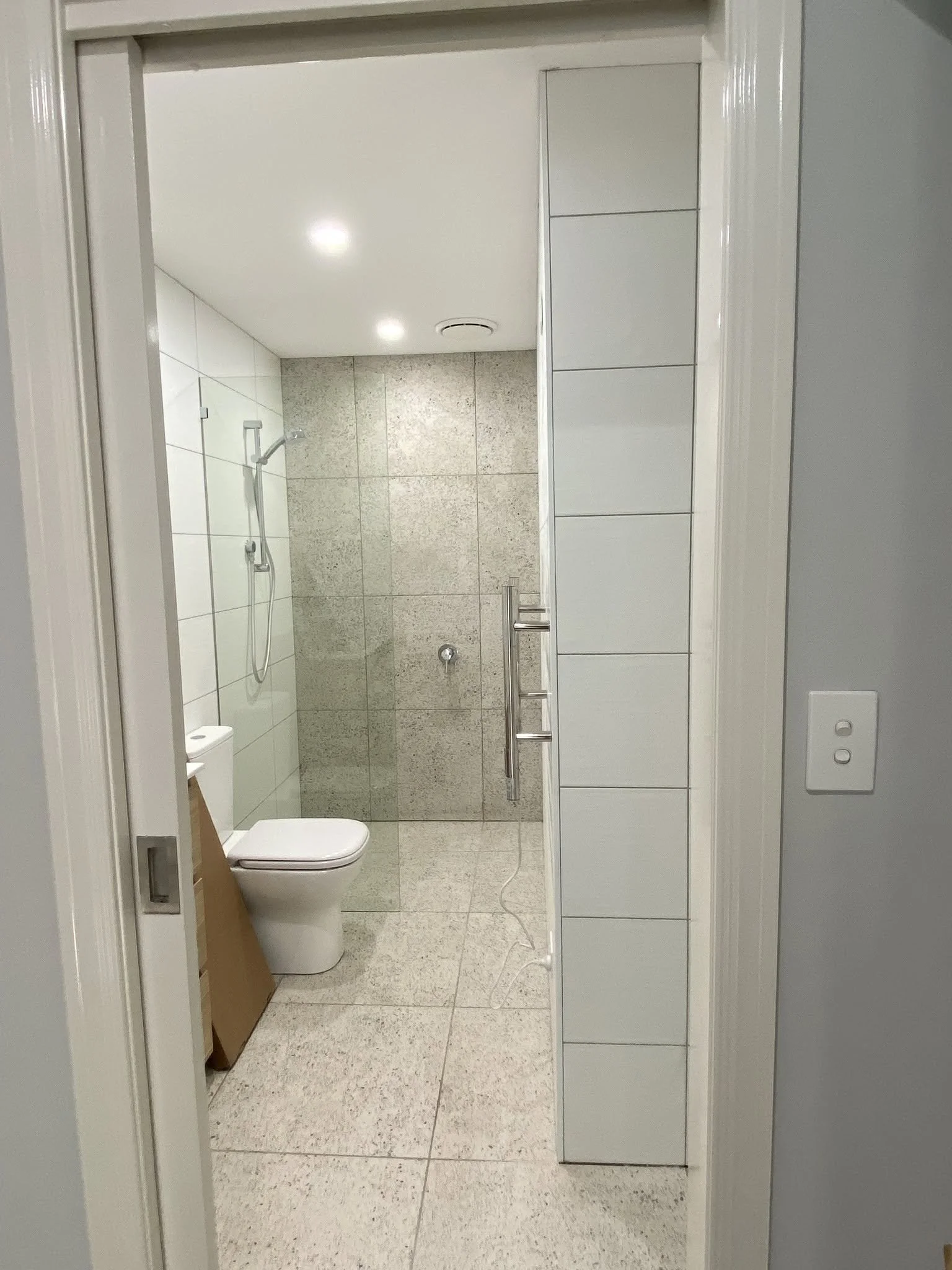 New bathroom with large grey tiles, a walk-in shower with a rail shower and a toilet