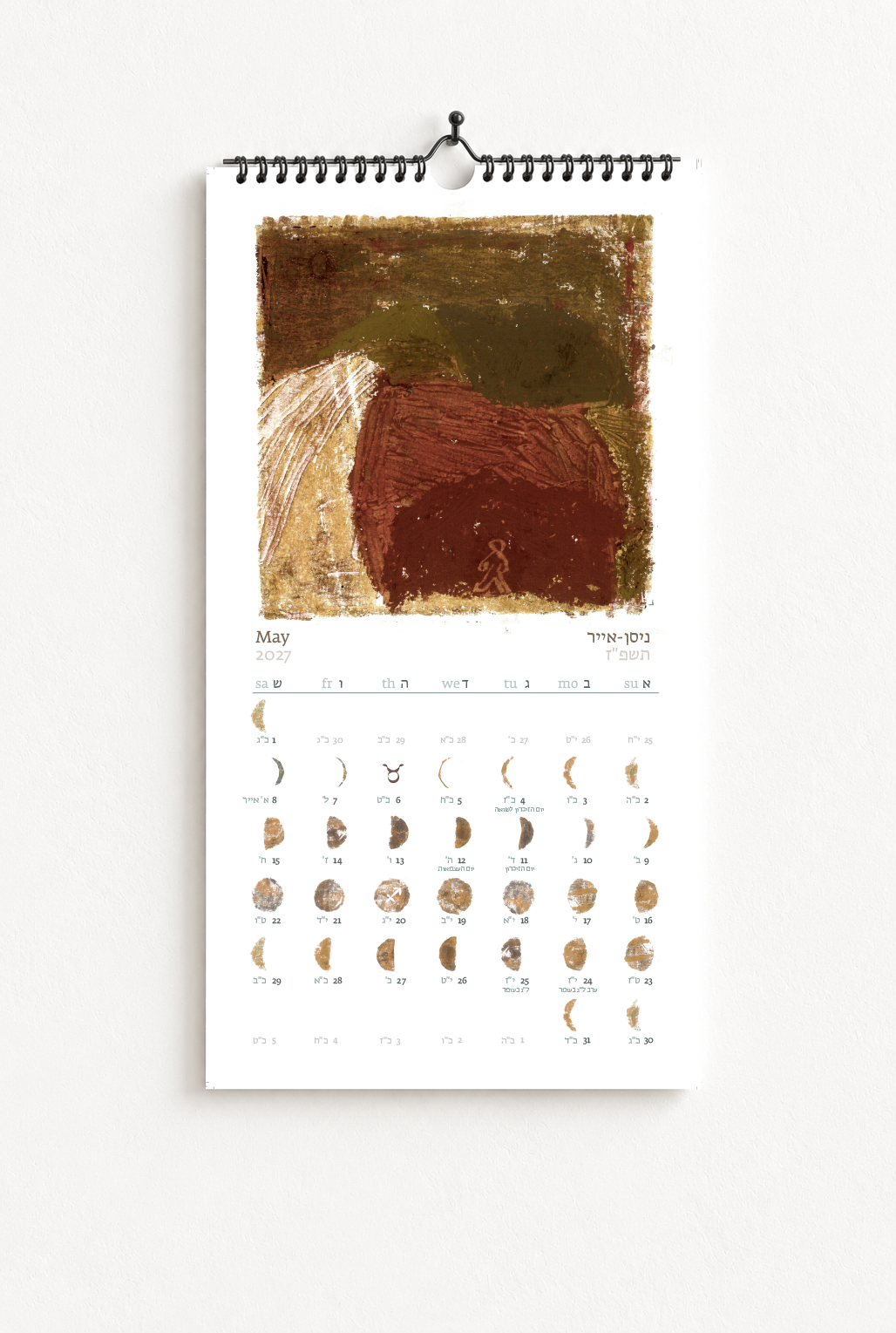 A wall calendar for May 2023 featuring abstract artwork with earthy tones. The calendar displays days and Hebrew dates, with a small drawing of a person near the center.
