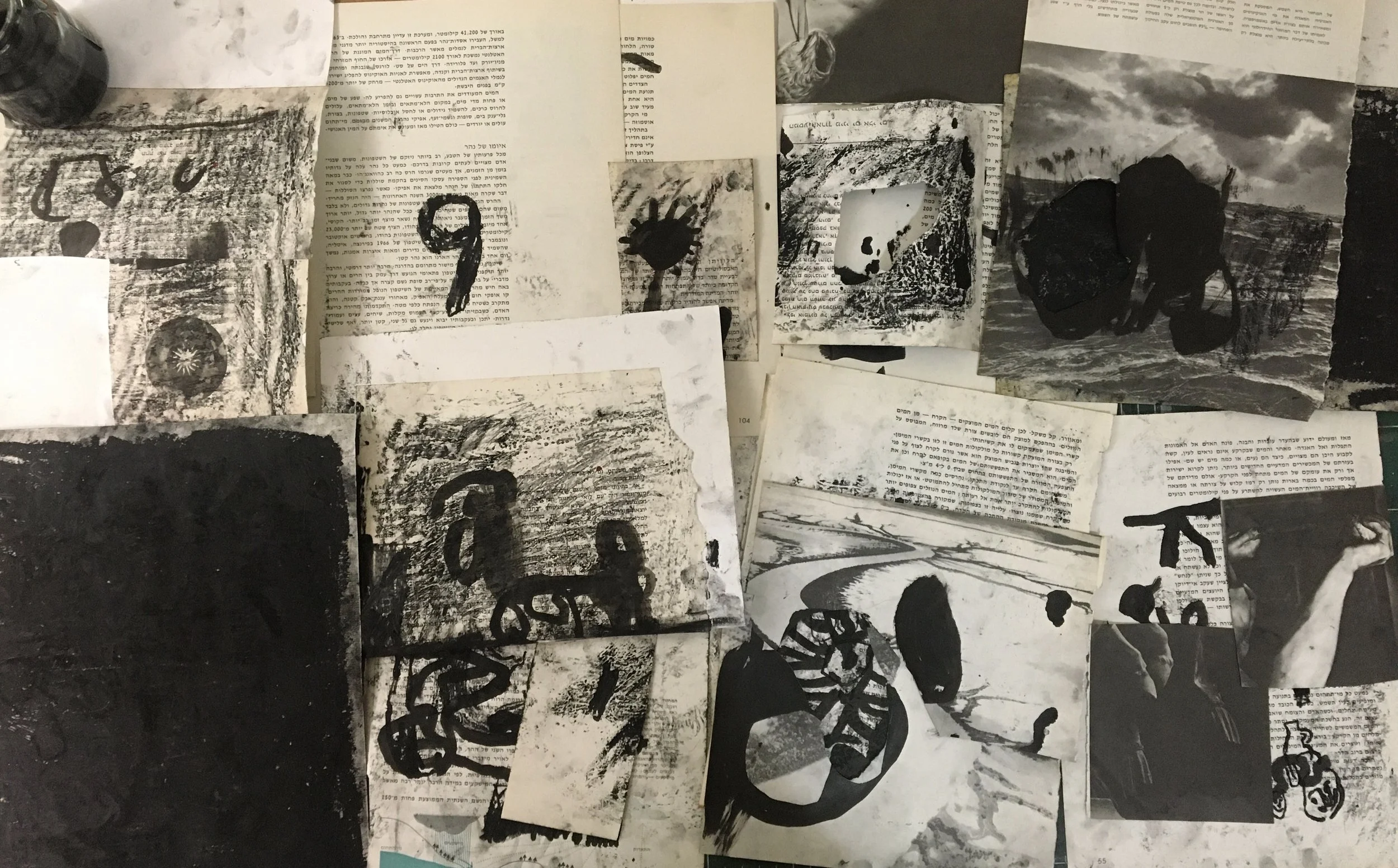 A cluttered desk with various black and white photographs, printed texts, and abstract artwork scattered across the surface.