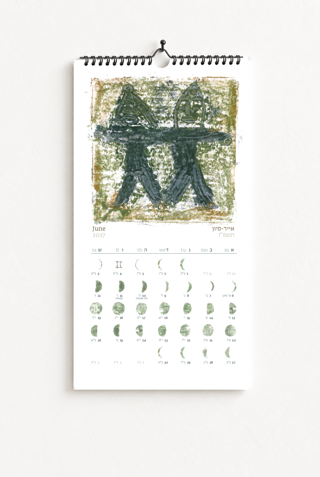 A wall calendar for June 2023 featuring artwork of two stylized figures holding a plank or branch. The calendar has Hebrew and English labels with lunar phases.