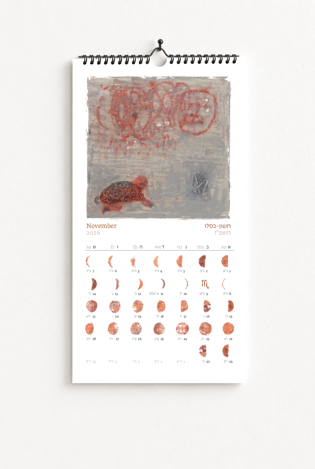A wall calendar for November 2026 with artwork featuring a turtle, abstract red shapes, and Hebrew text, displayed on a white wall.
