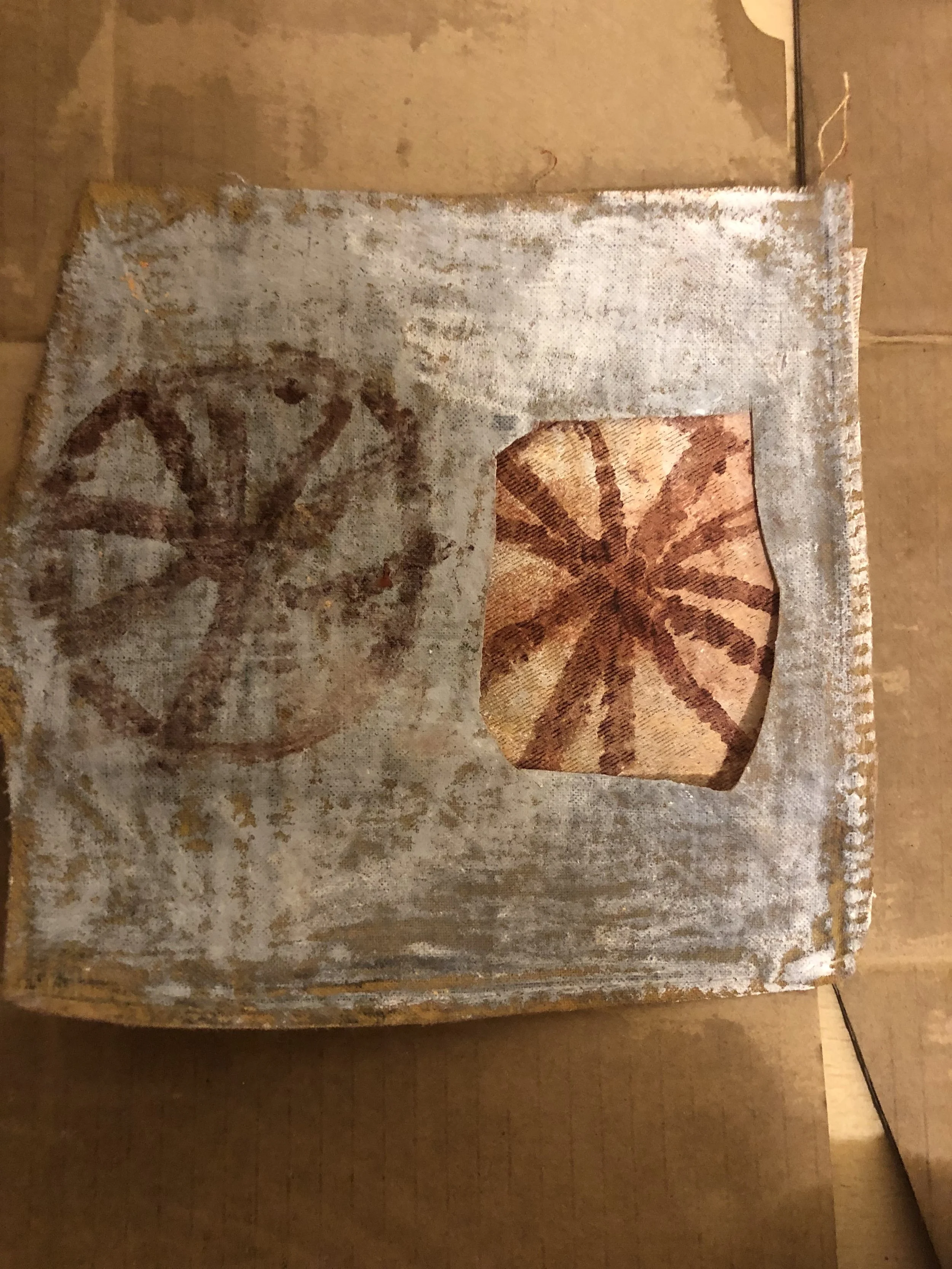 A rusty metal surface with two painted lotus flower designs, one faded and the other more vivid, against a tan background.