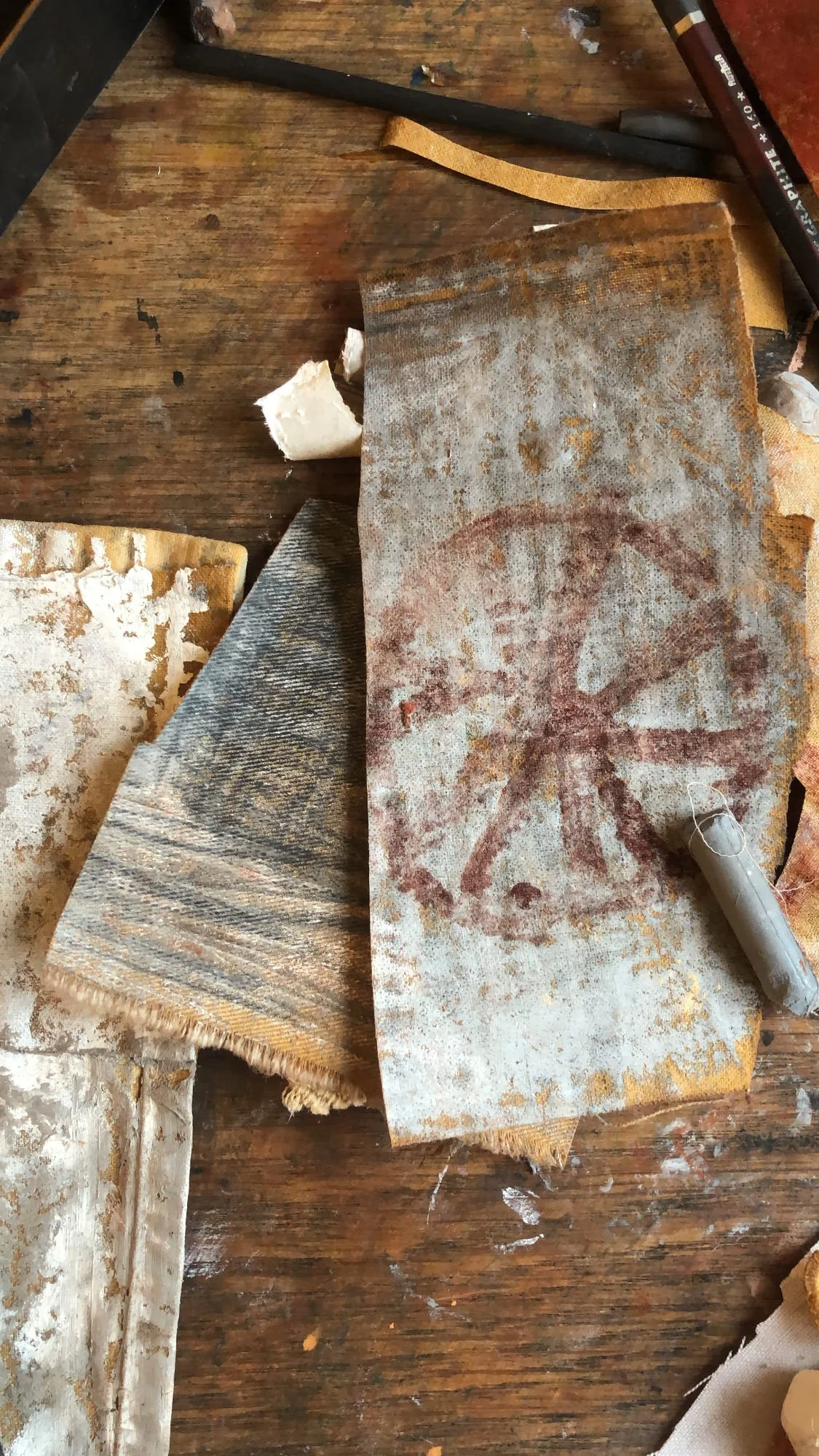 A worn and stained piece of fabric or paper, some chalk, and various tools on a wooden surface.