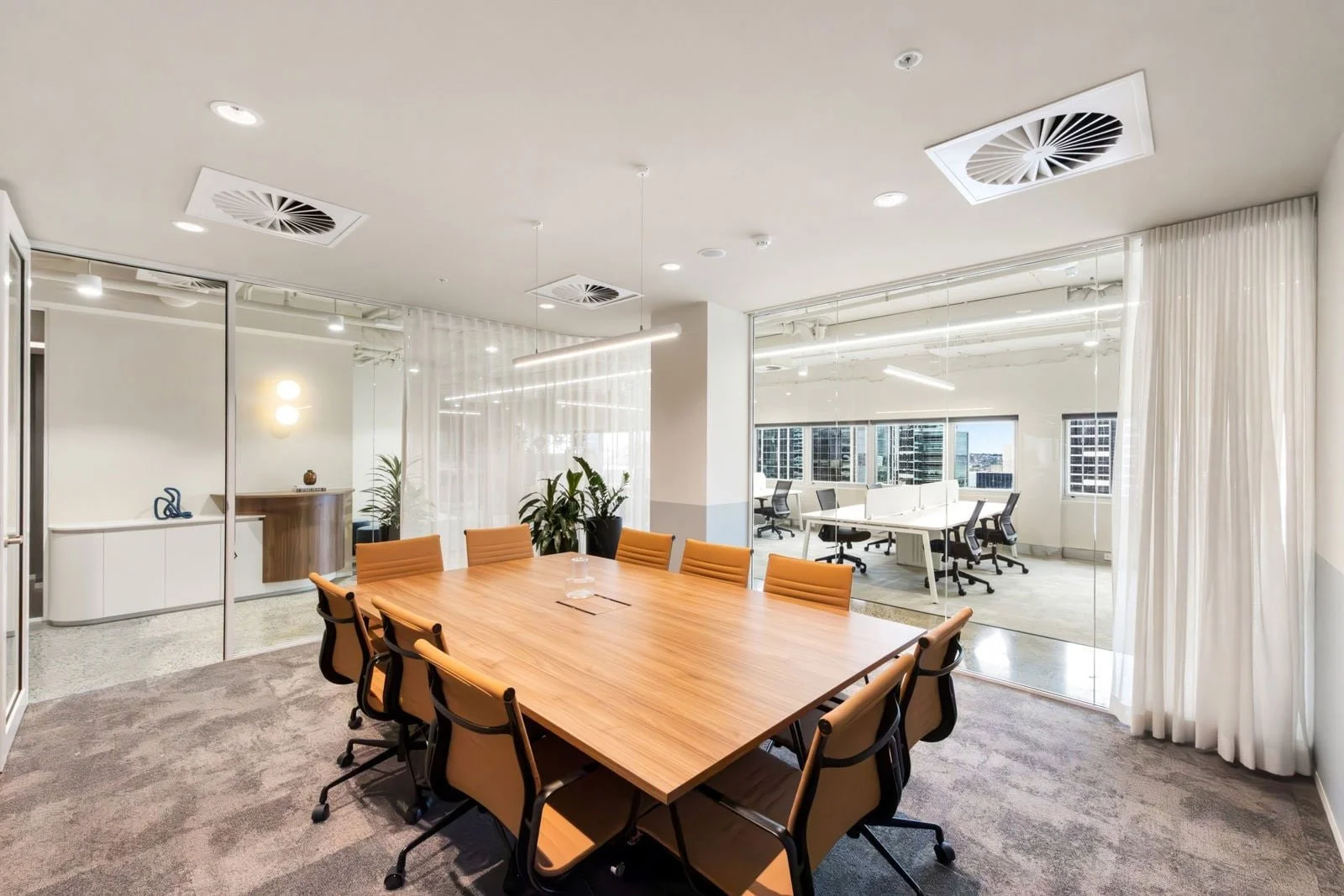 Modern conference room with wooden table, beige chairs, glass wall, and a view of open office space with white desks and black chairs