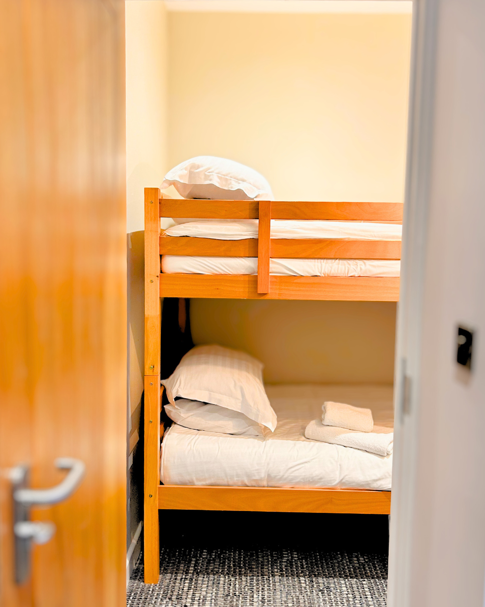 View of a wooden bunk bed with two beds, pillows, and folded towels in a small room.