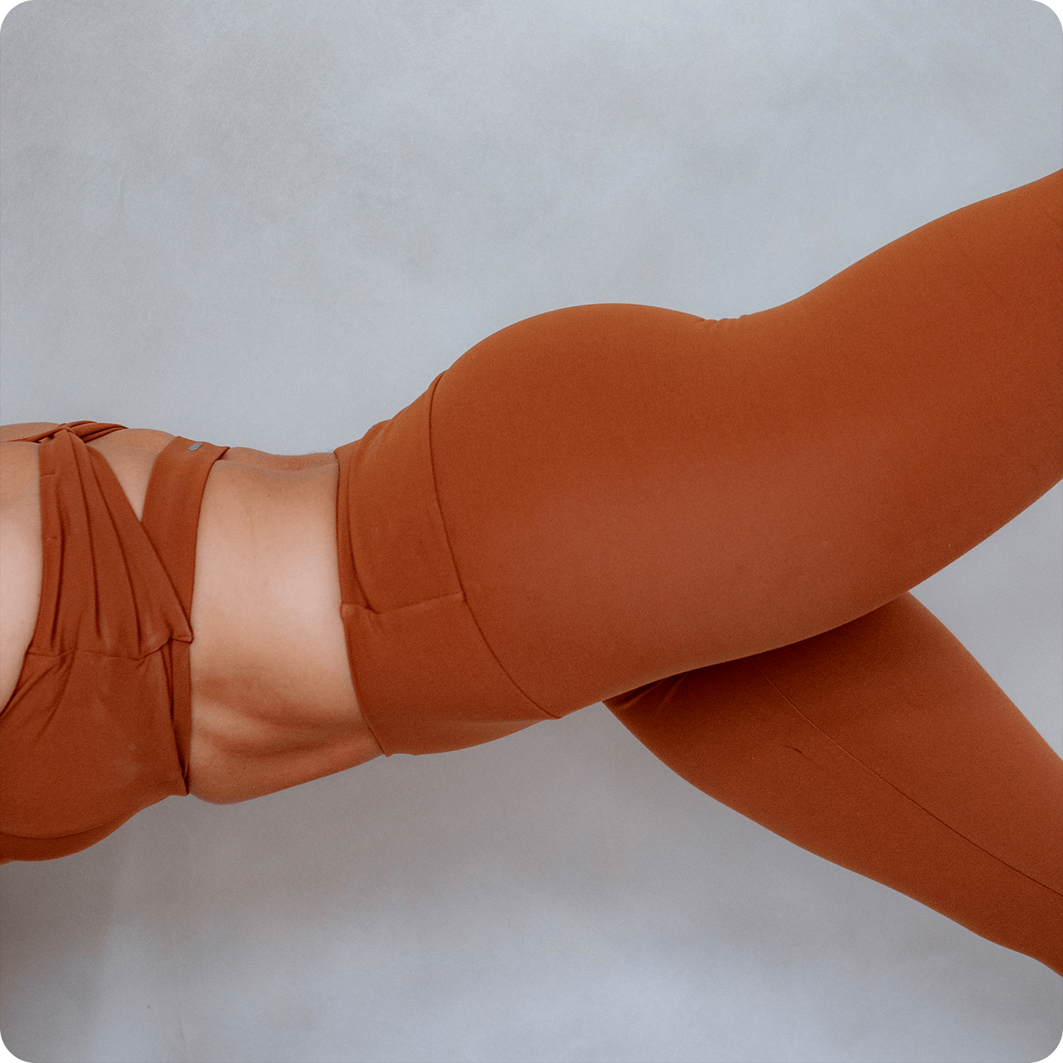 Close-up of a woman in tan activewear, lying down with her legs crossed, against a plain light background.