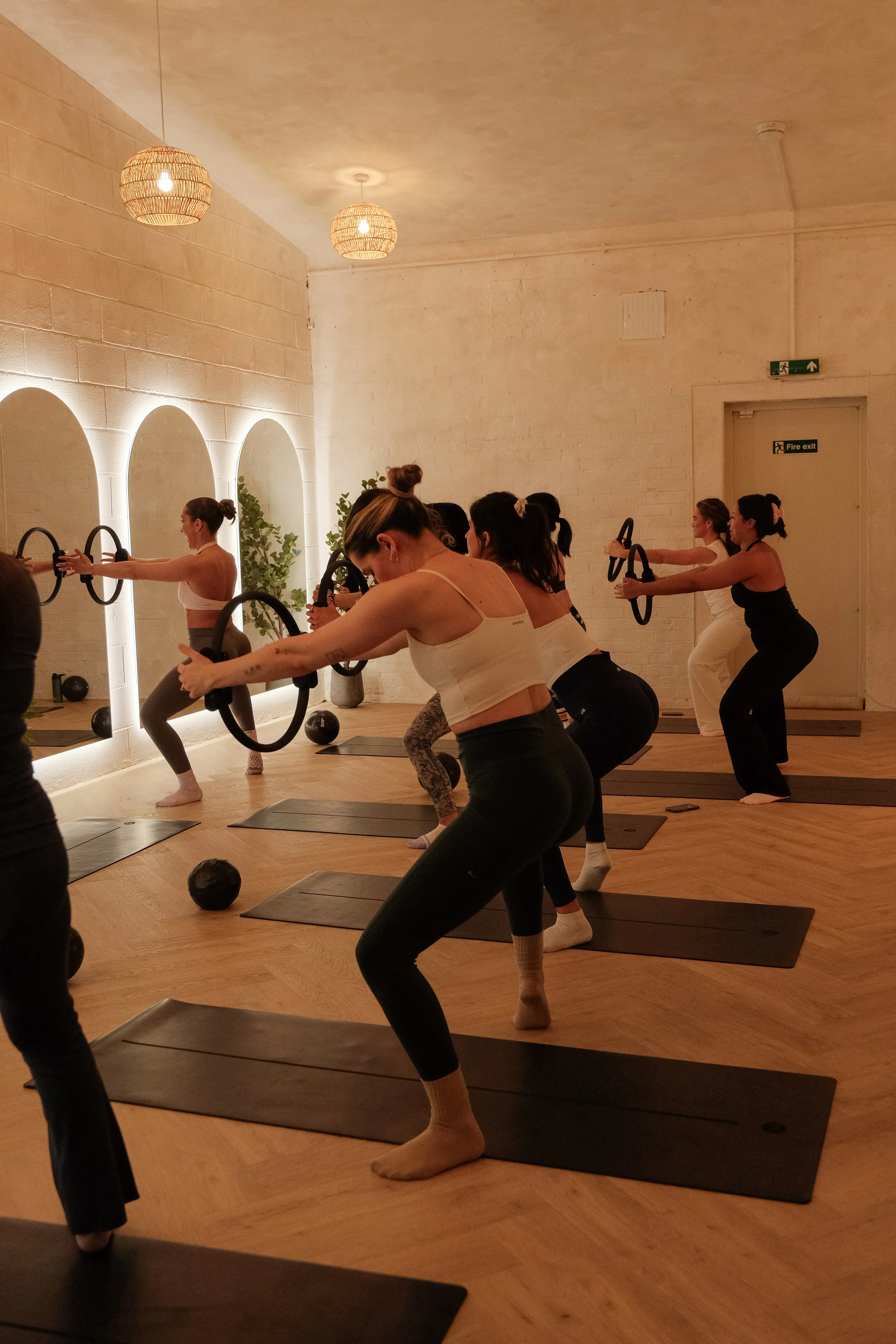 Women participating in a fitness class focusing on squats using fitness rings, in a brightly lit room with a mirror and wall decor.