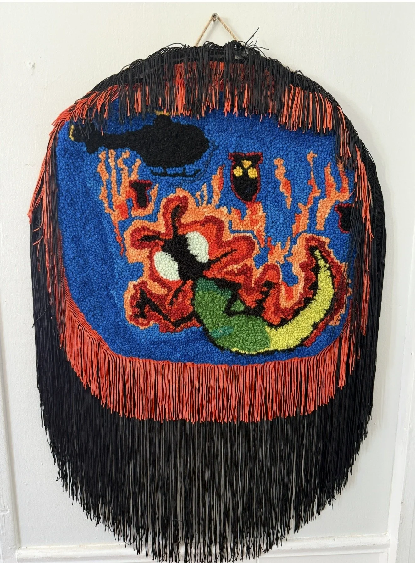 A colorful, circular  wall hanging featuring acreature with yellow eyes