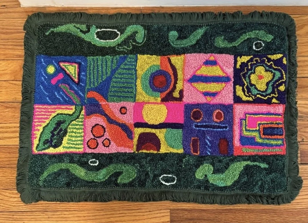 Colorful geometric abstract design on a rectangular rug with a green fringe border.